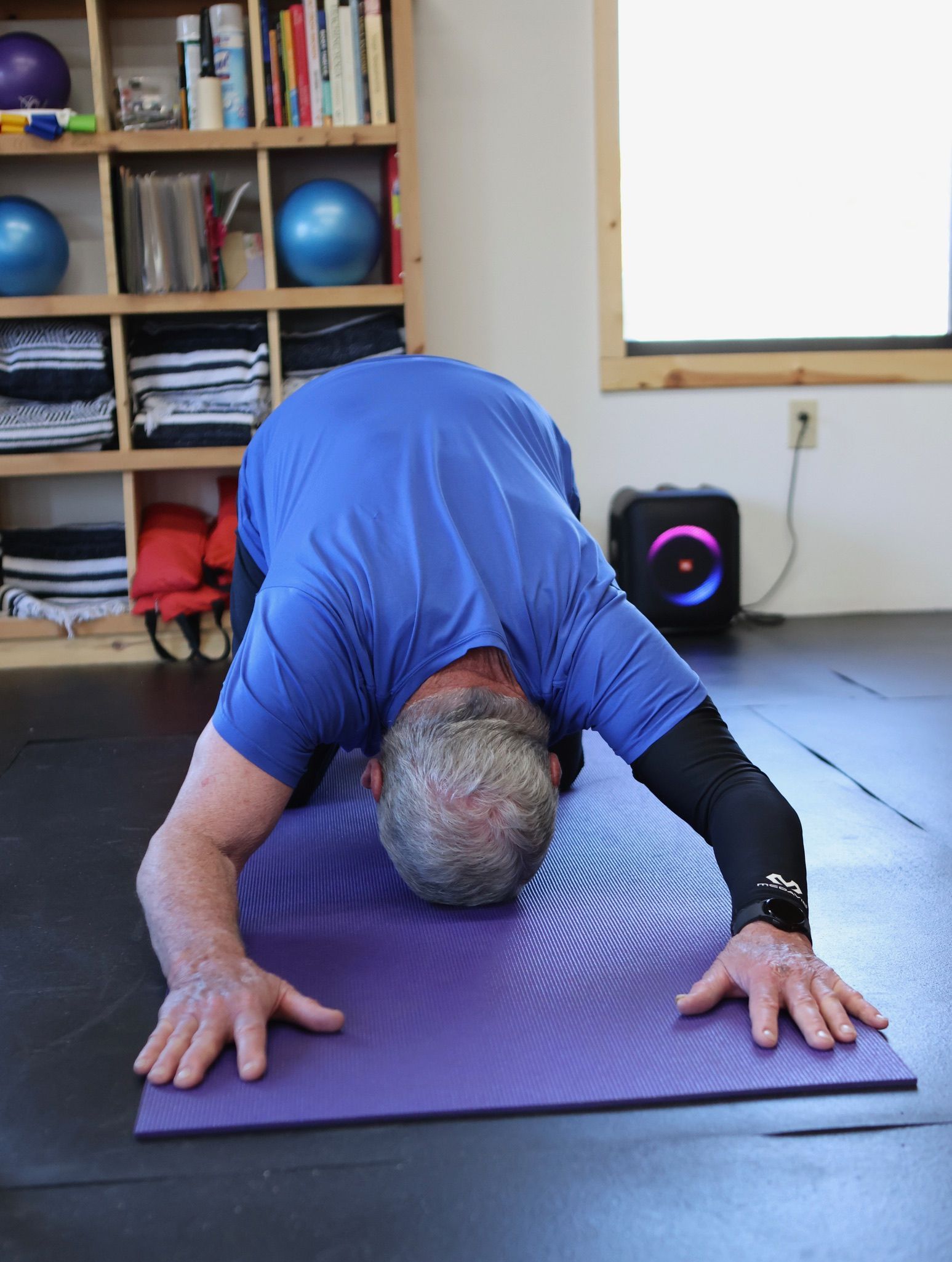 A man in a blue shirt is doing a yoga pose on a purple mat