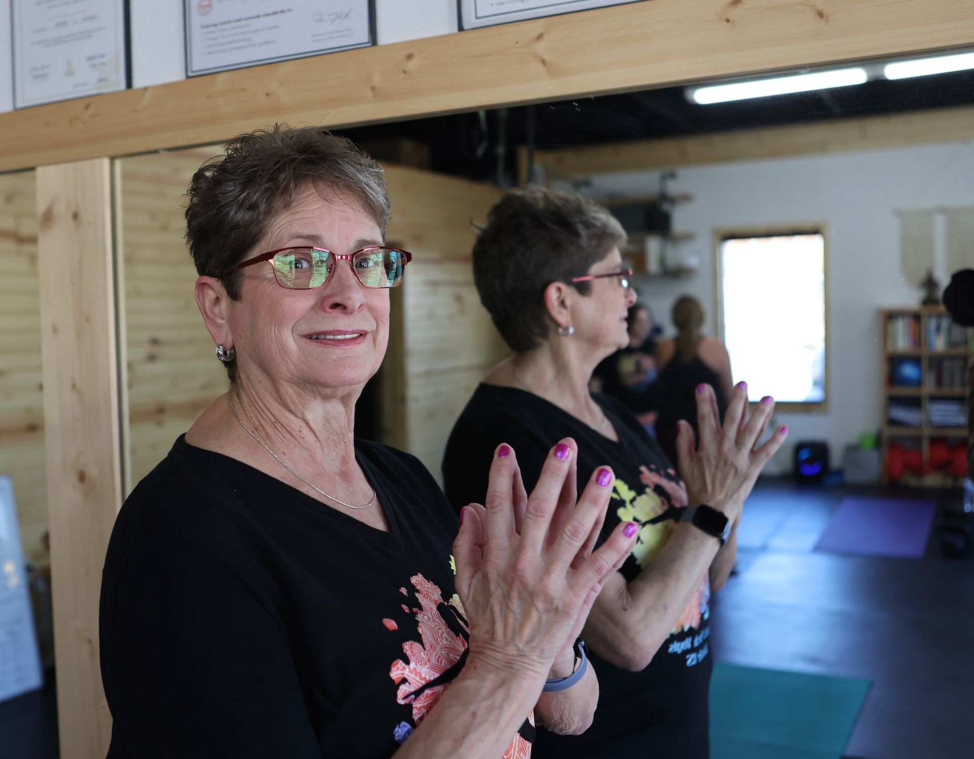 A woman wearing glasses is clapping her hands in front of a mirror.