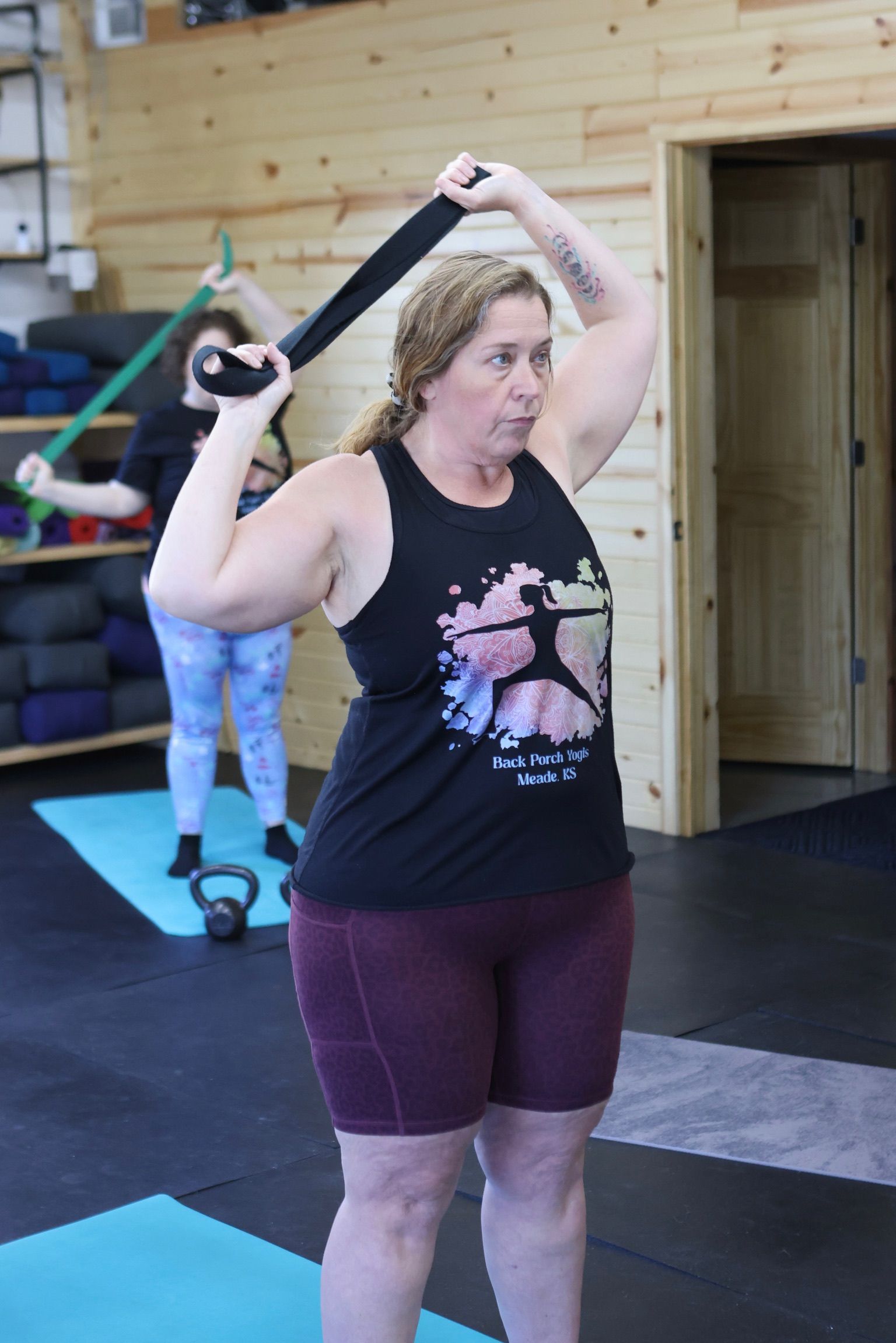A woman is holding a resistance band over her head in a gym.