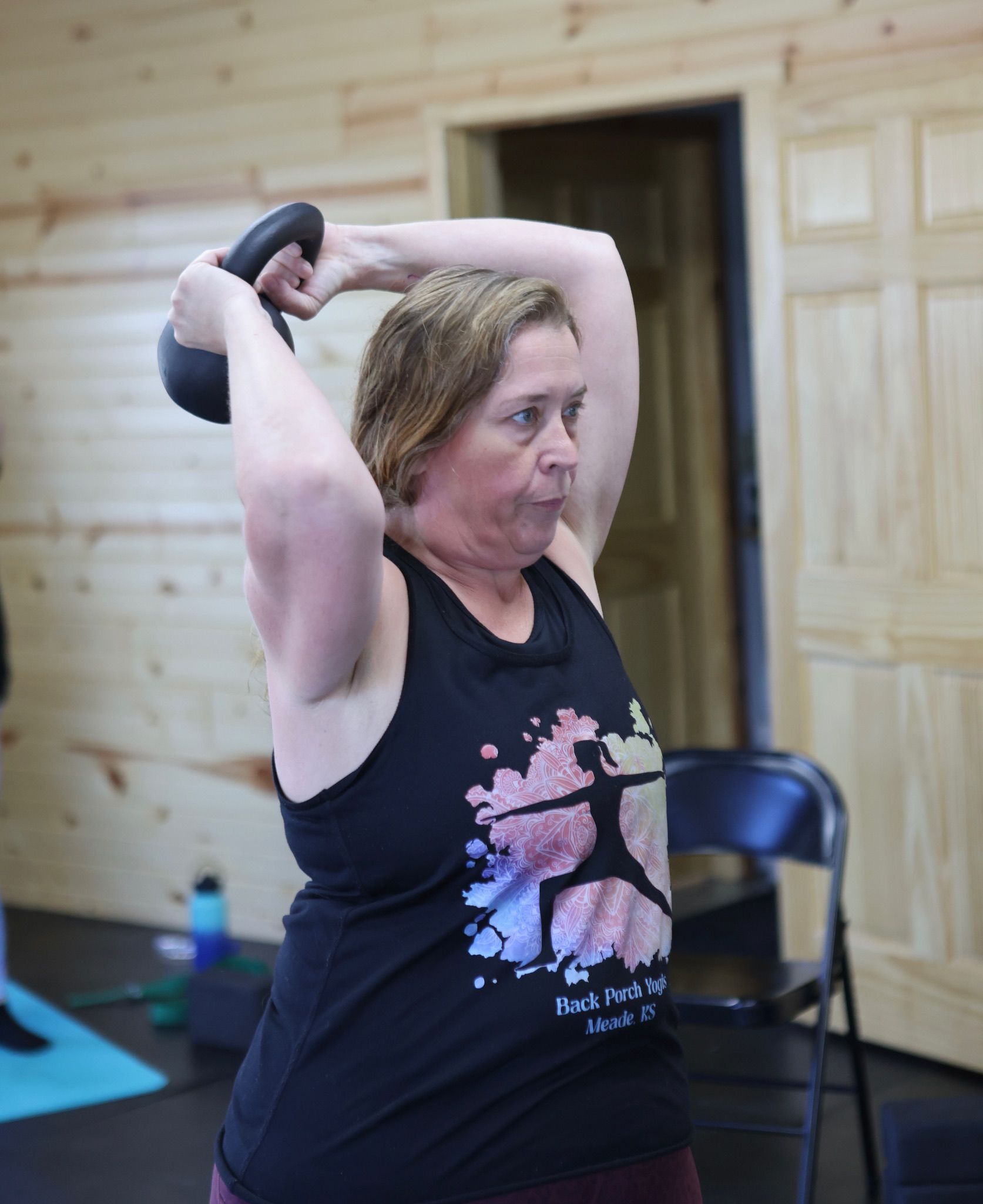 A woman is holding a kettlebell over her head in a gym.