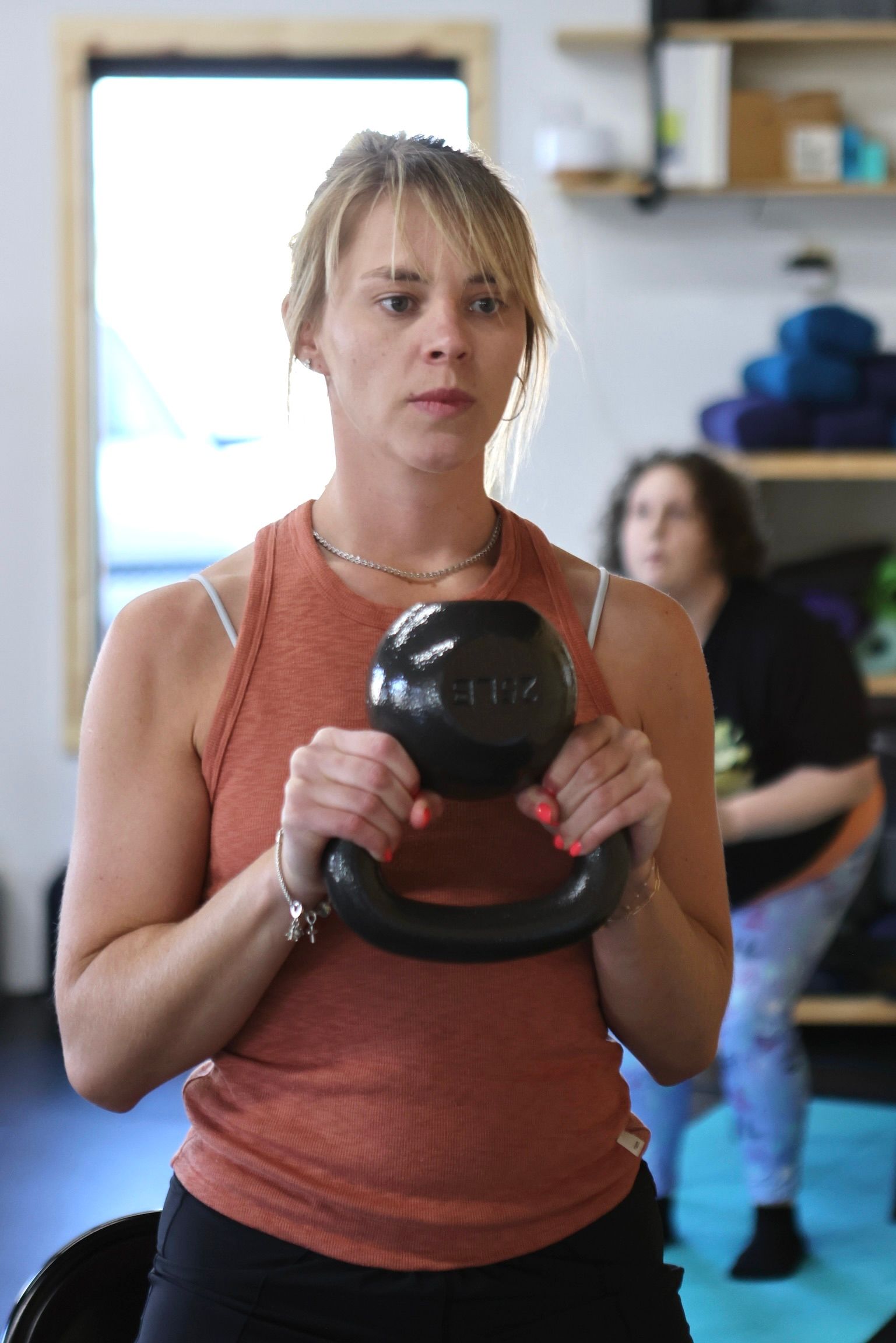 A woman is holding a kettlebell in her hands in a gym.