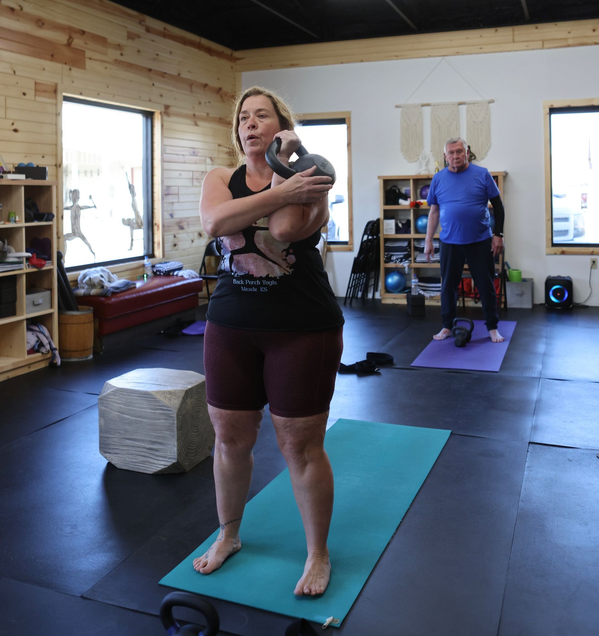A woman is standing on a yoga mat holding a kettlebell