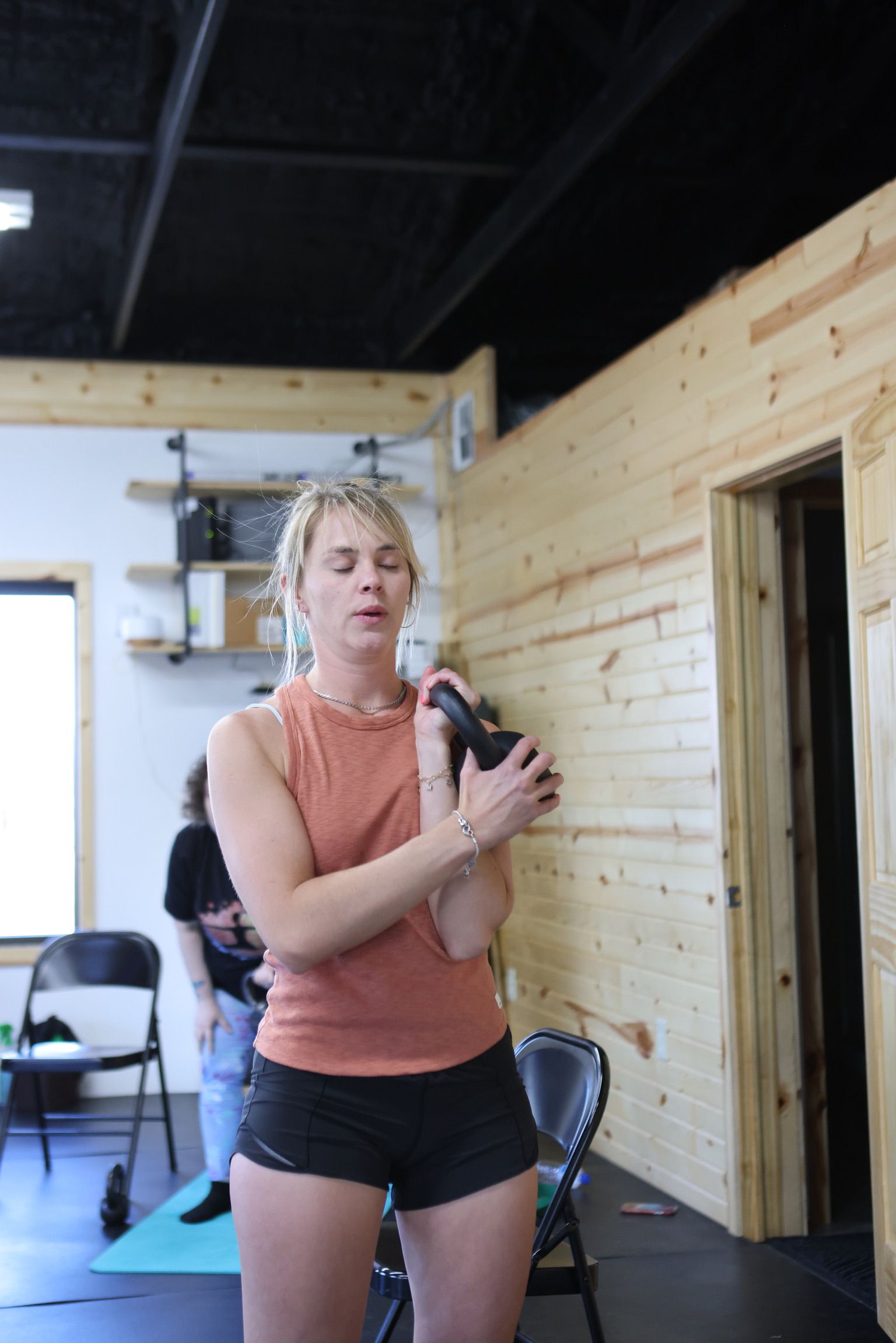 A woman is standing on a yoga mat in a gym holding a dumbbell.
