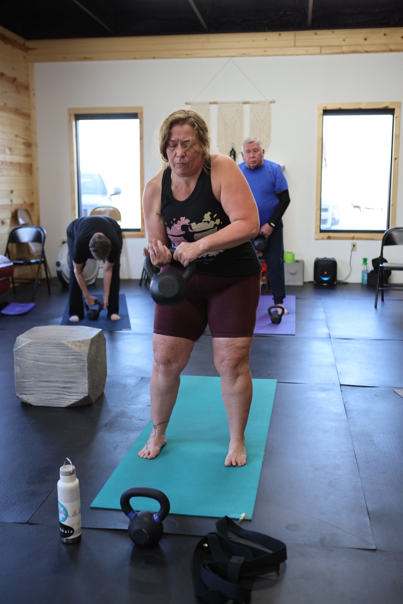 A woman is standing on a yoga mat holding a kettlebell.