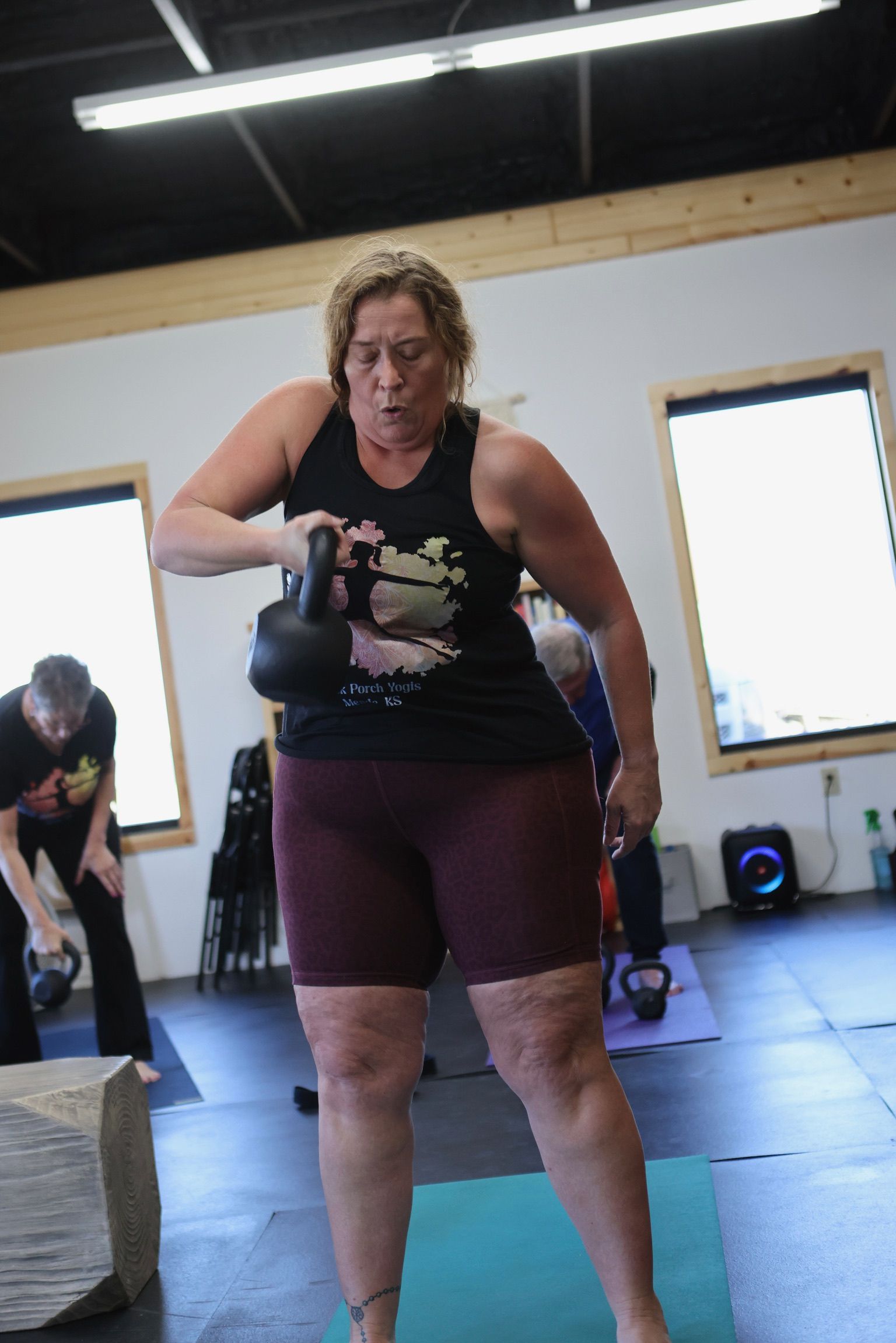 A woman is standing on a yoga mat holding a kettlebell.