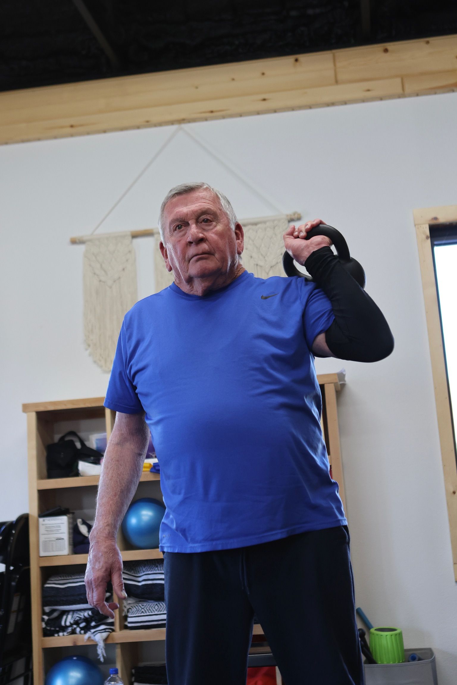 A man in a blue shirt is holding a kettlebell in a gym.