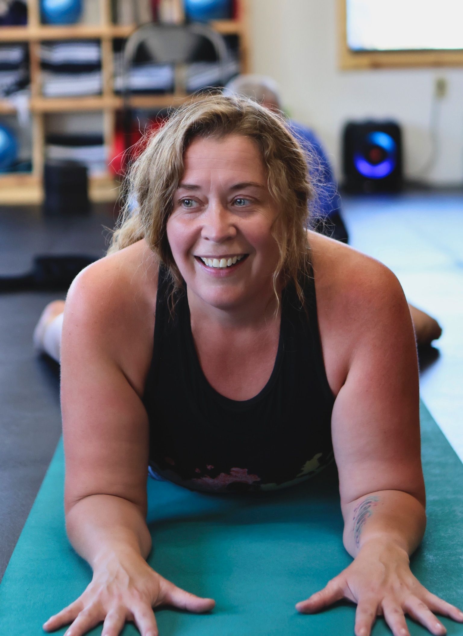 A woman is smiling while laying on a yoga mat in a gym.