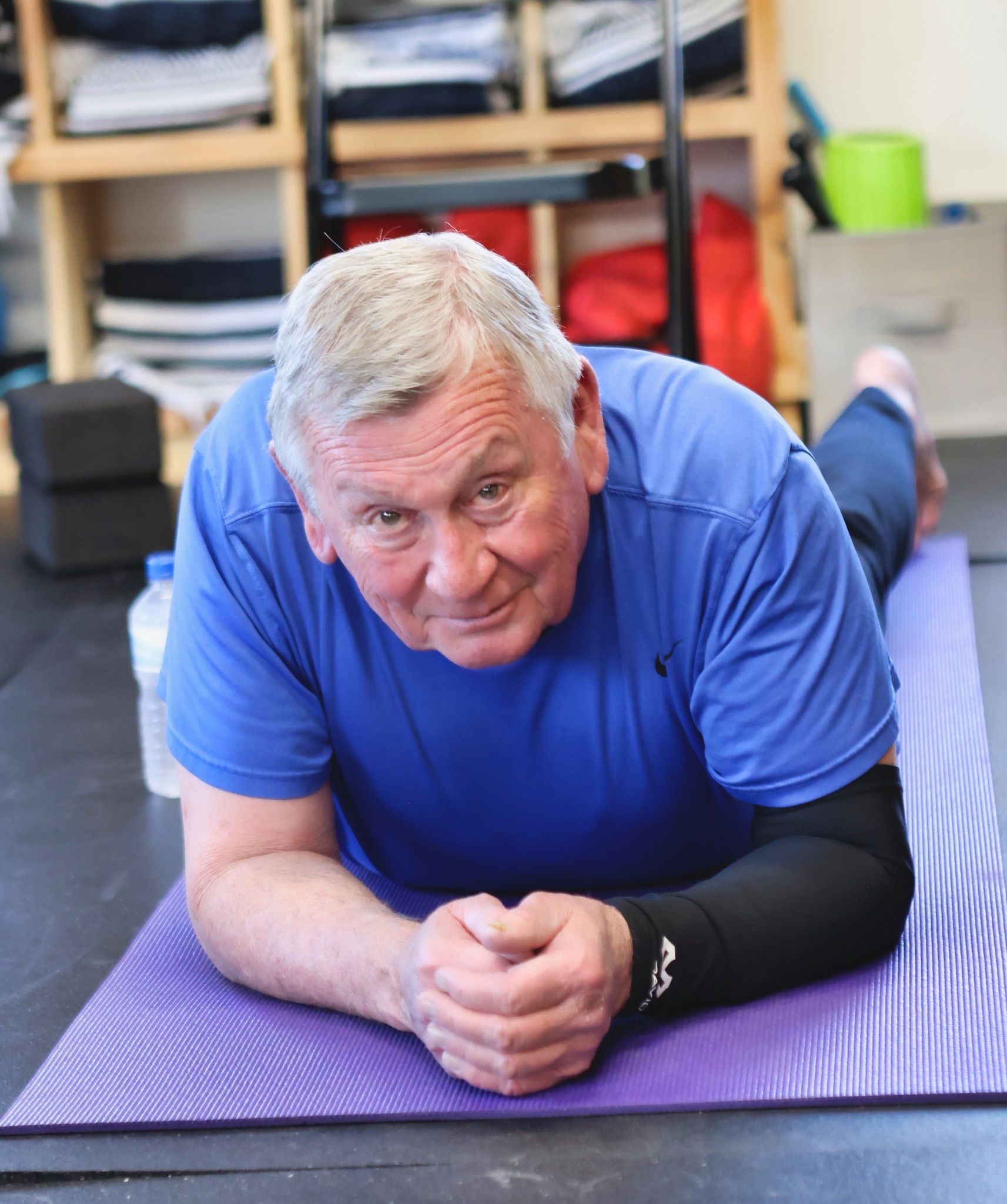 A man in a blue shirt is laying on a yoga mat