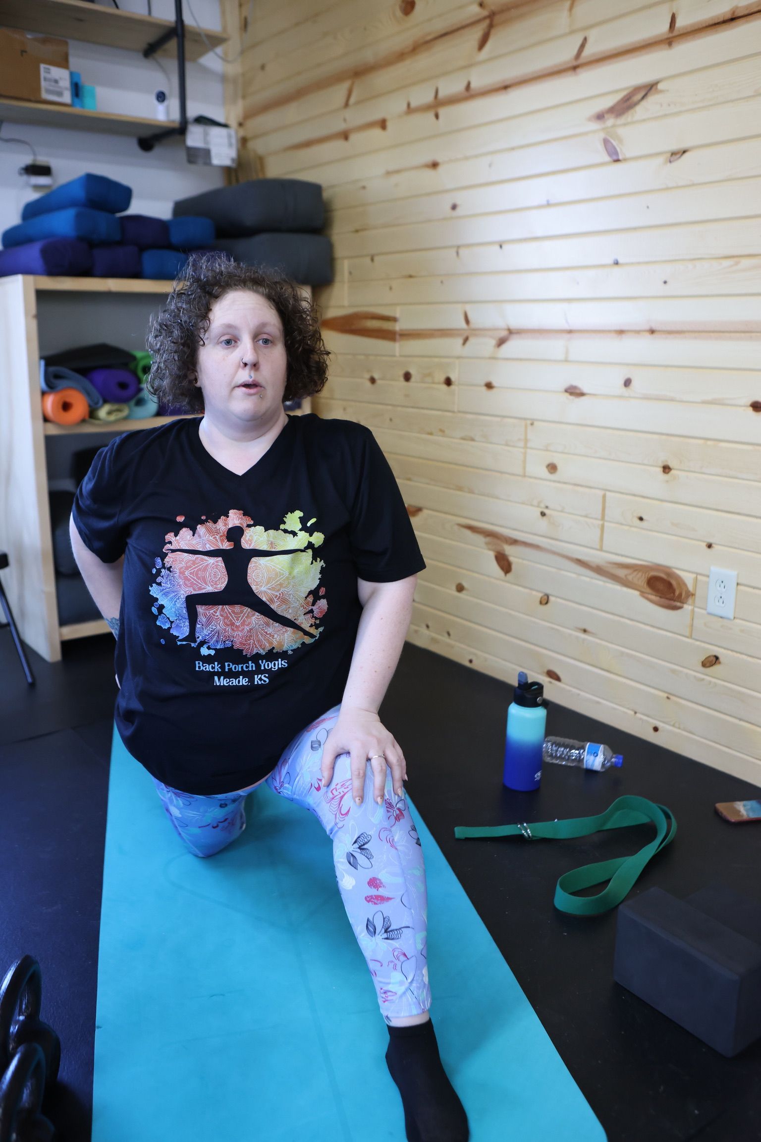 A woman is sitting on a yoga mat in a room.