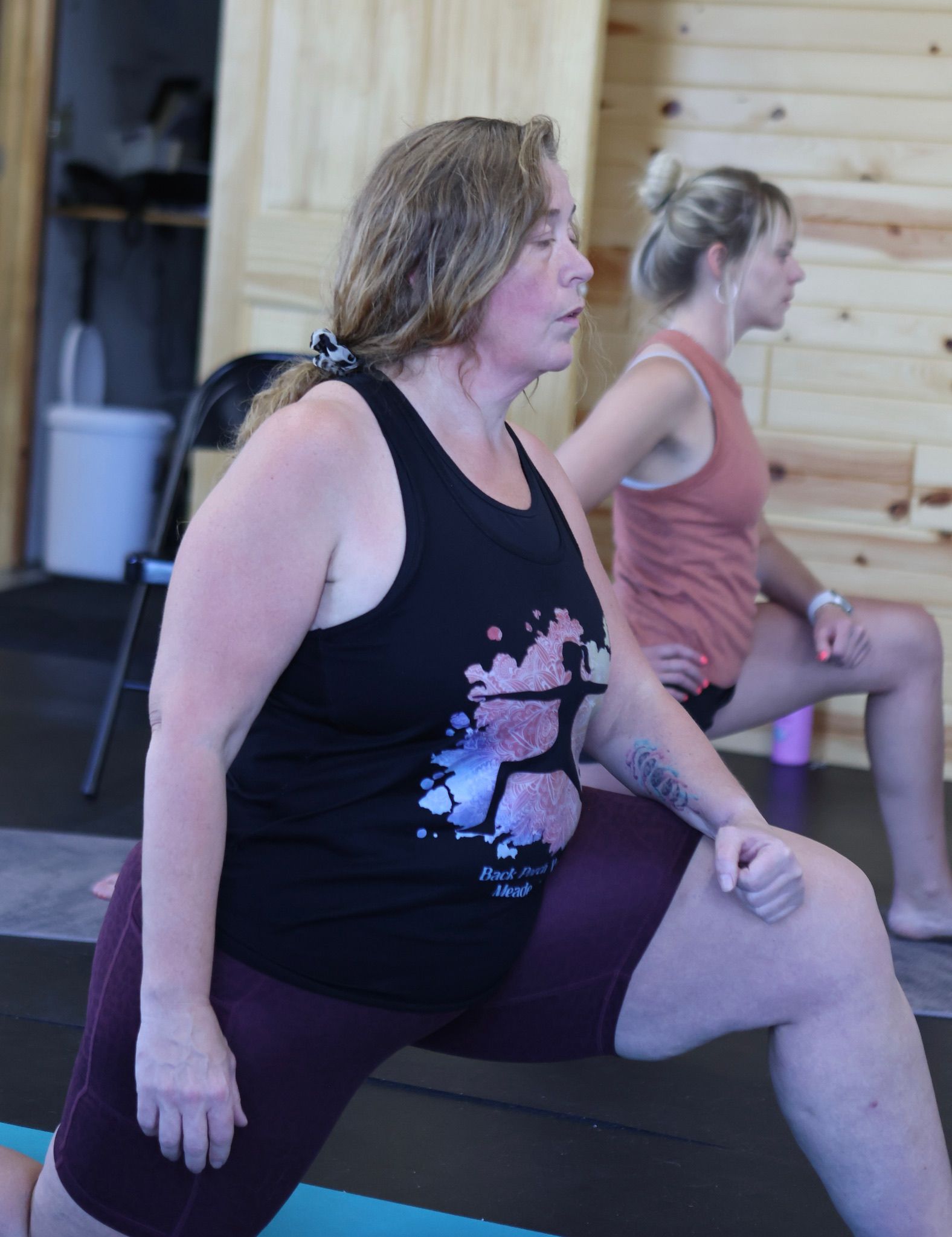 A woman in a black tank top is stretching on a yoga mat