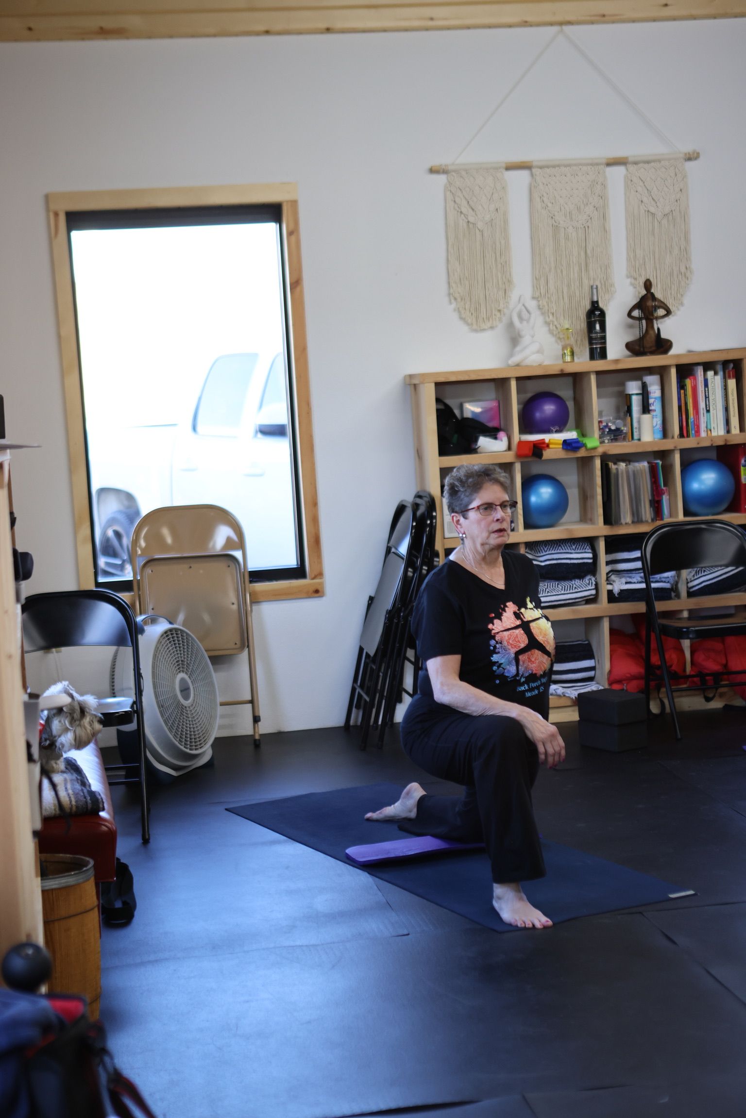 A woman is kneeling on a yoga mat in a room.