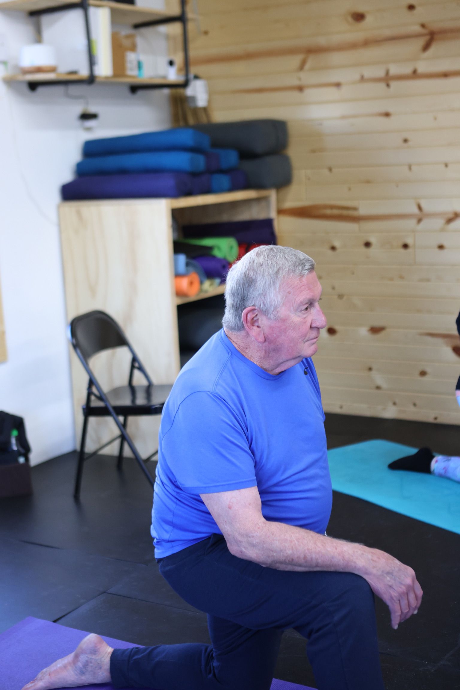 A man in a blue shirt is kneeling on a yoga mat