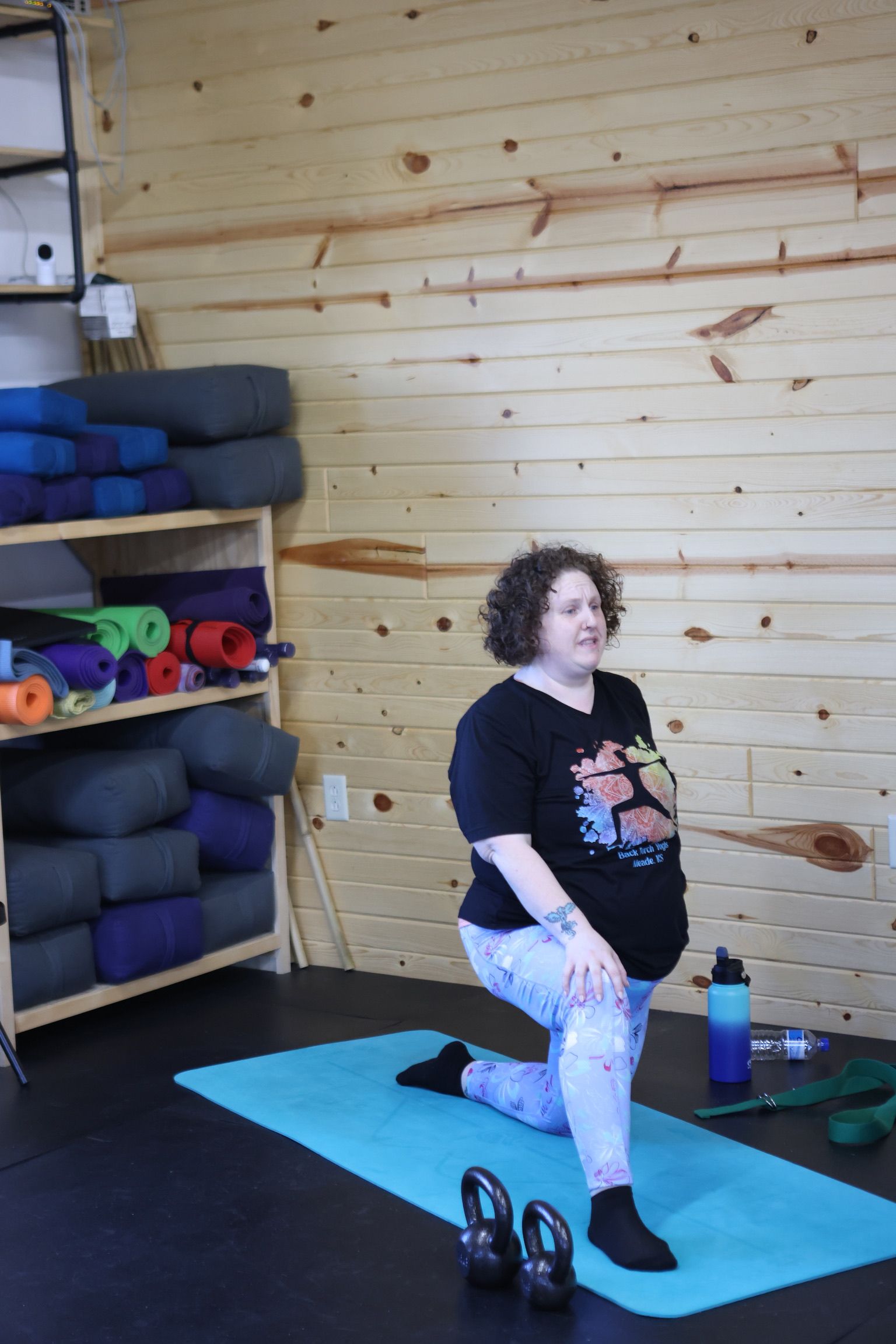 A woman is kneeling on a yoga mat in a room.