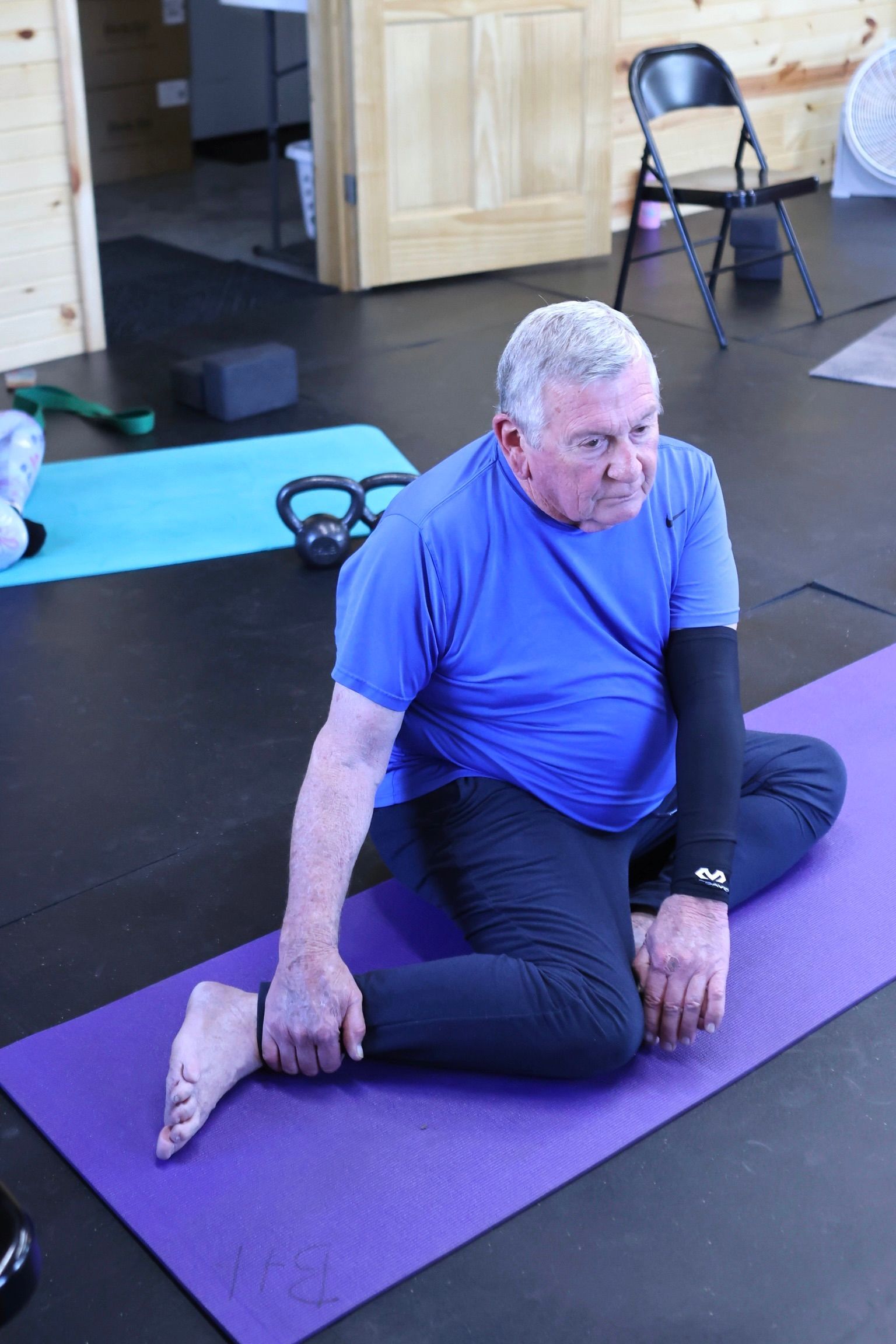 A man in a blue shirt is sitting on a purple yoga mat.