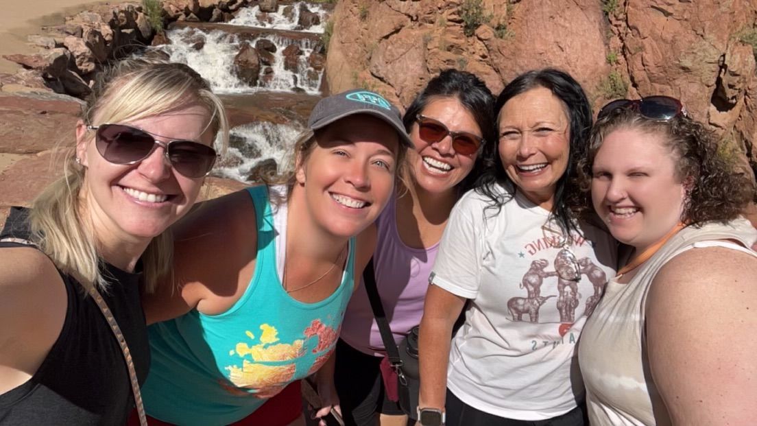 A group of women are posing for a picture in front of a waterfall.