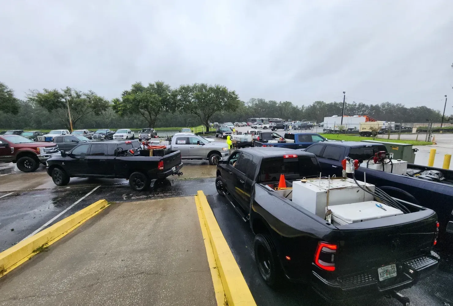 Black pickup trucks and other vehicles parked at a facility on a wet, overcast day.