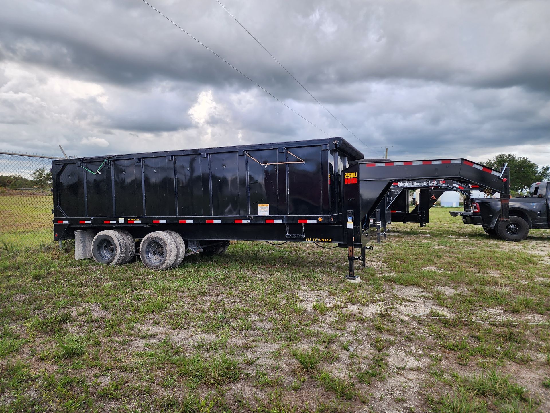 Green truck lifting a blue dumpster in front of a brick building on a snowy day.