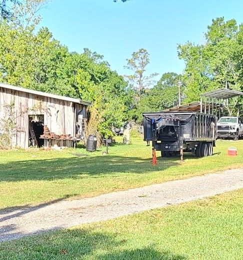 A weathered wooden building and a large black dump trailer sit on a grassy property.