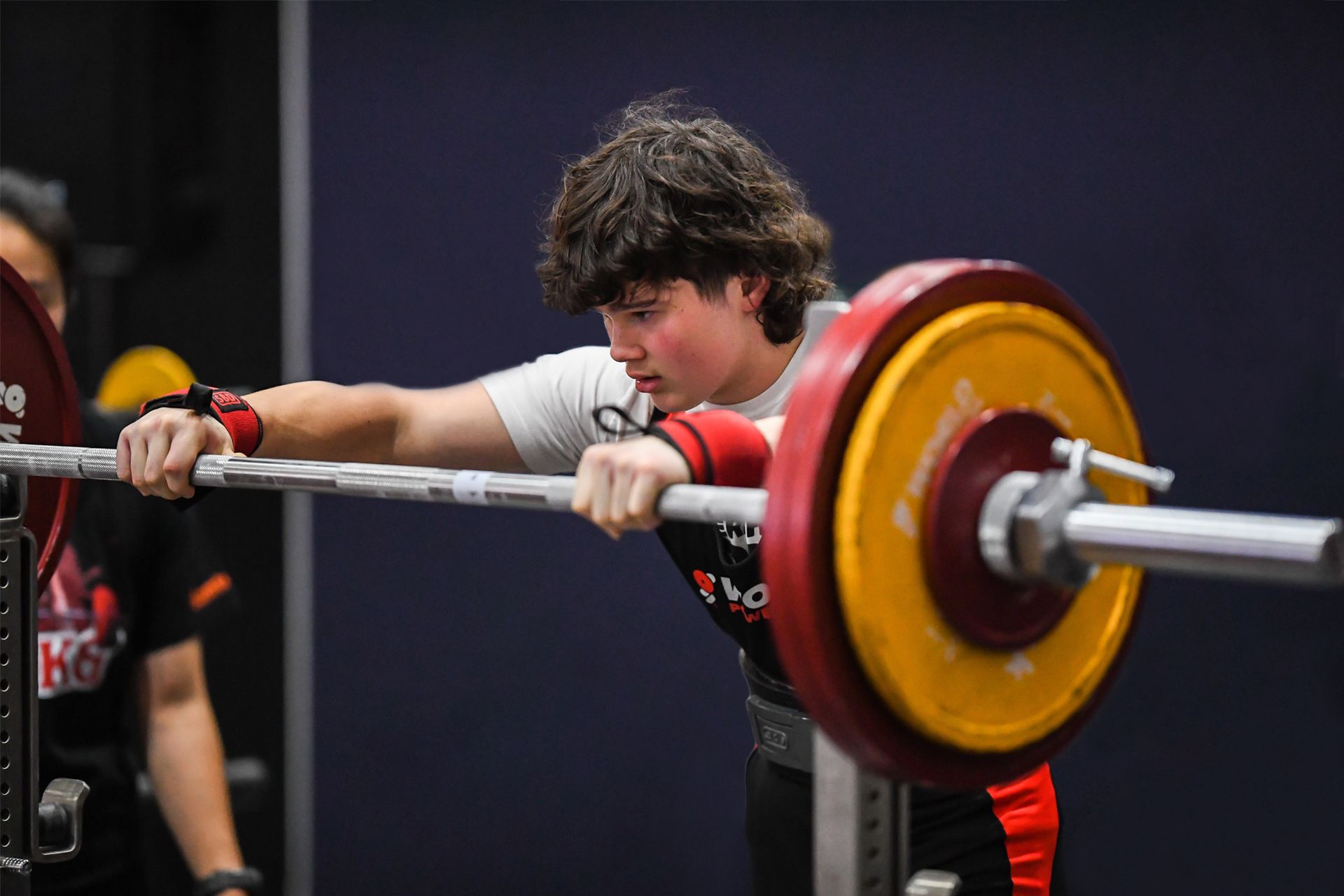 Young student athlete in white shirt and wrist wraps prepares to squat with a barbell.