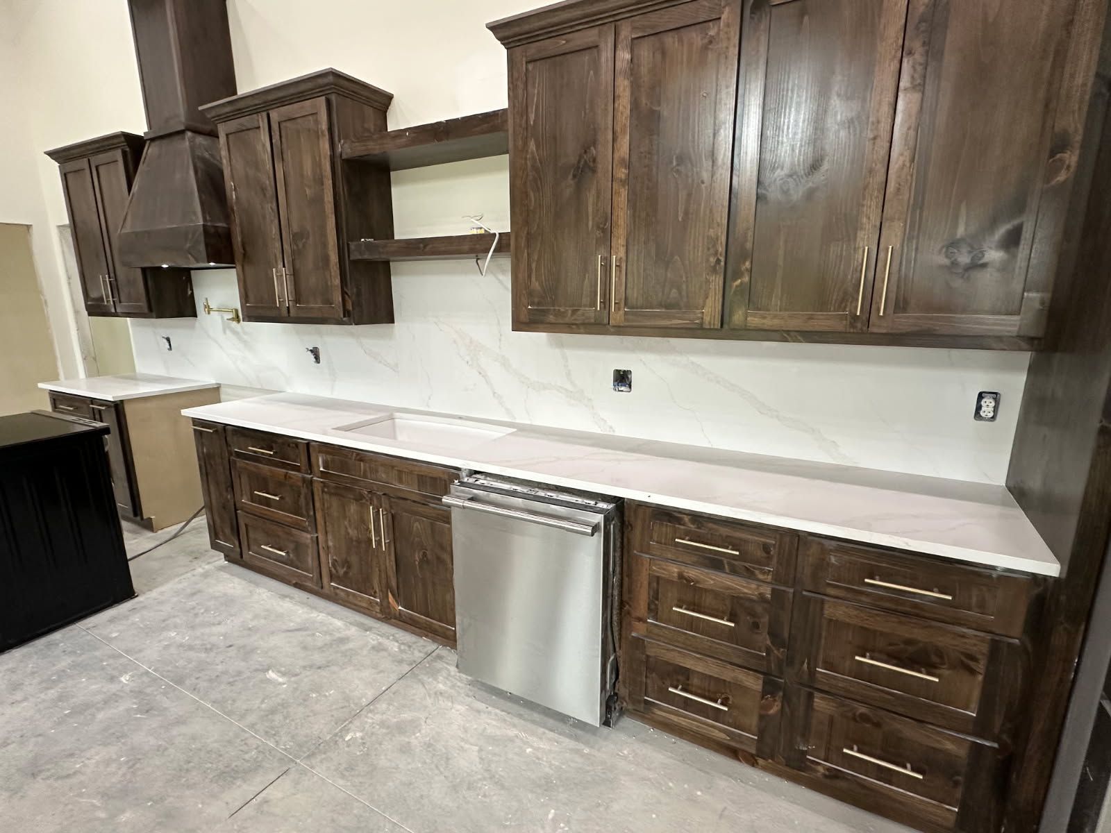 A kitchen with dark wood cabinets, white countertops, a stainless steel dishwasher, and a custom range hood.