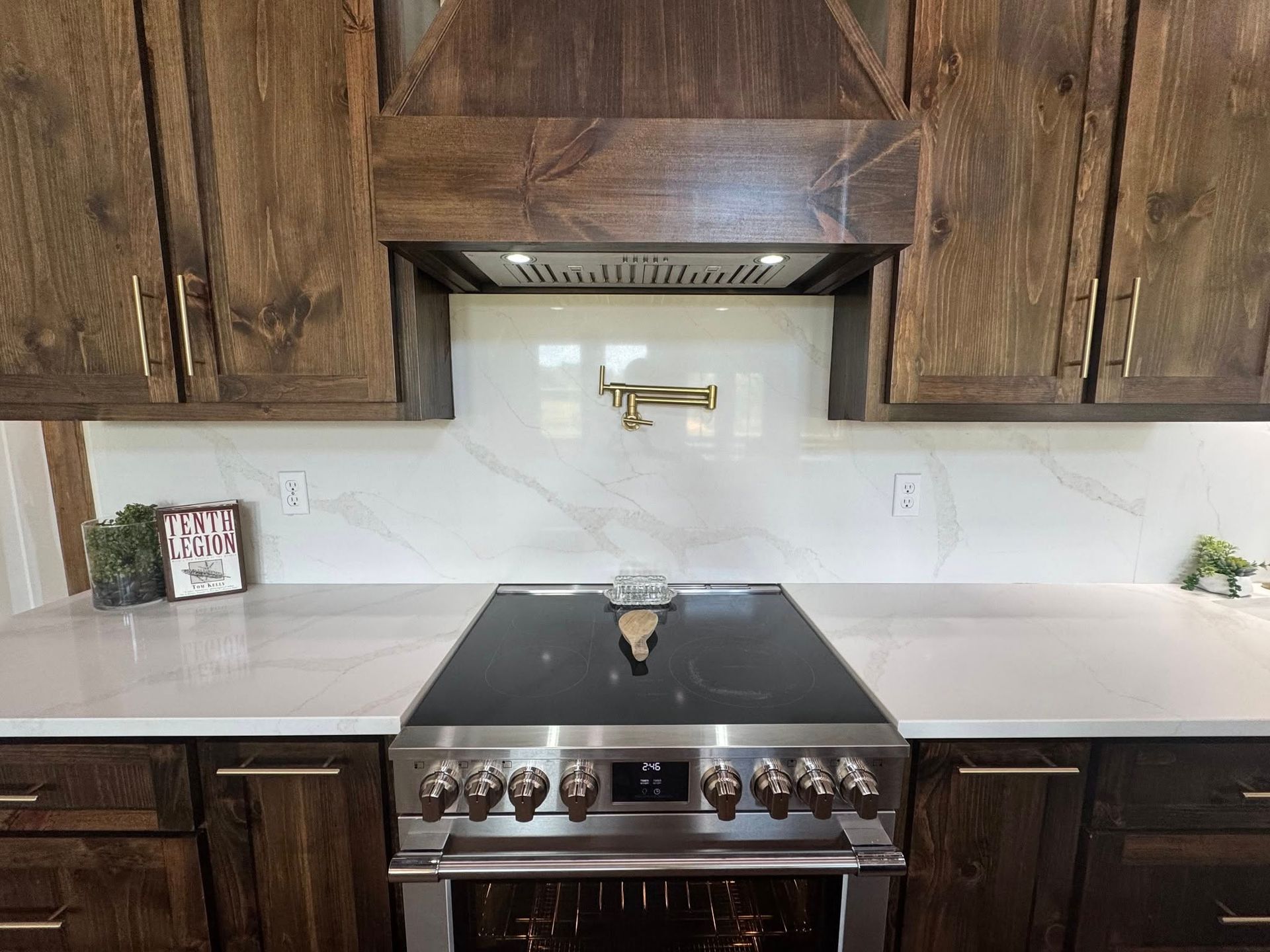 A kitchen stove with a pot filler faucet, white marble backsplash, and wooden cabinets under a matching vent hood.
