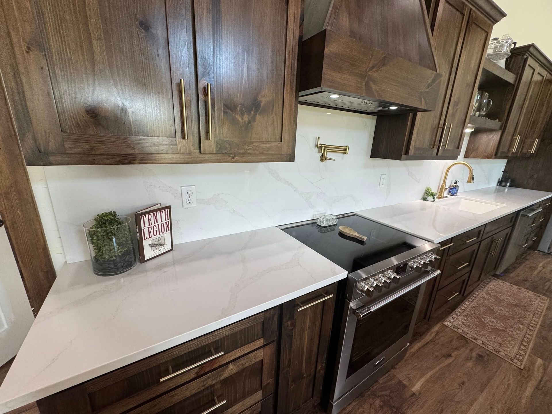 A kitchen with dark wood cabinets, white quartz countertops, a black stove, and a gold pot filler faucet on the backsplash.
