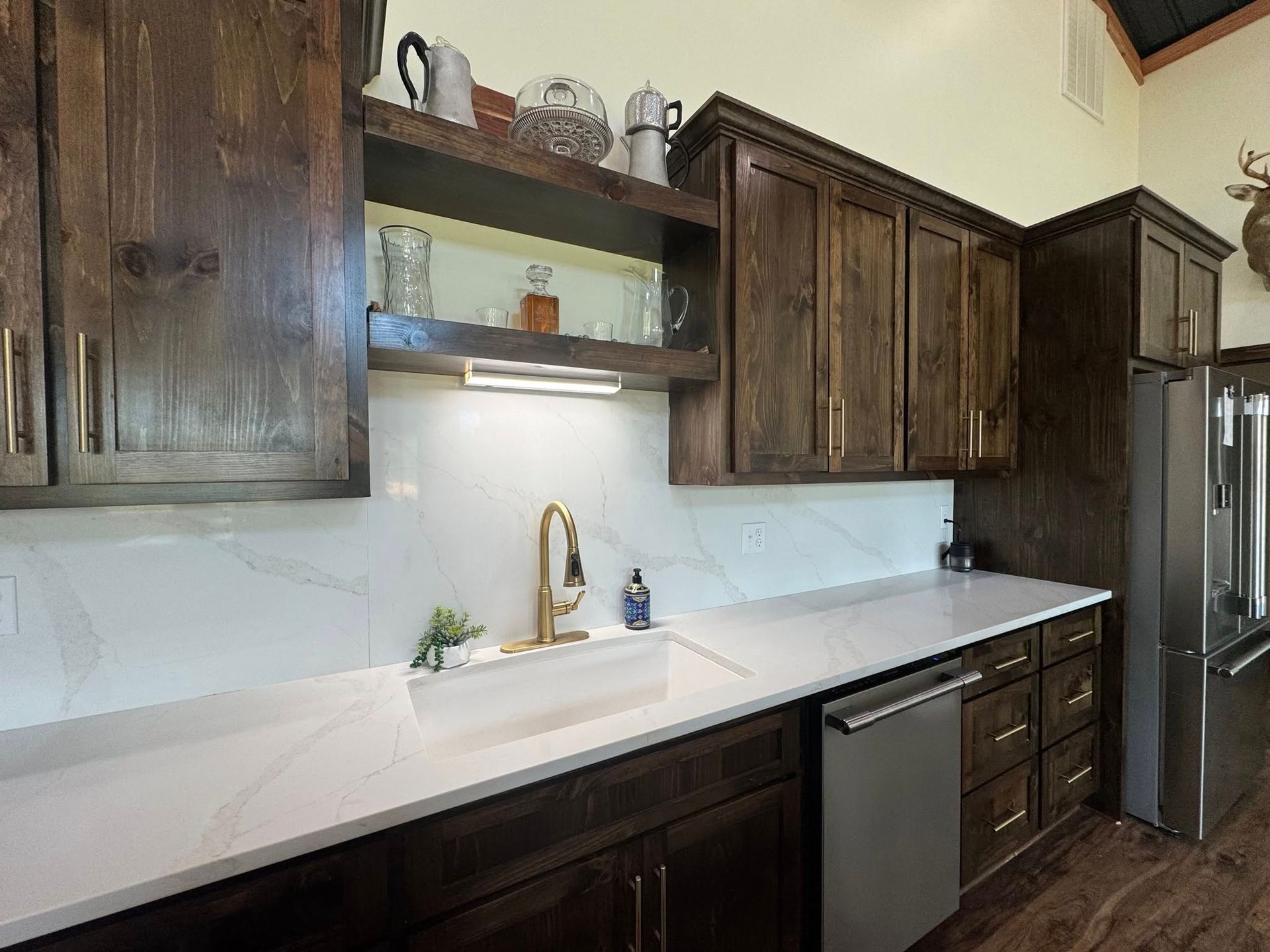 A kitchen featuring dark wood cabinets, white quartz countertops with a gold faucet, and a stainless steel dishwasher.