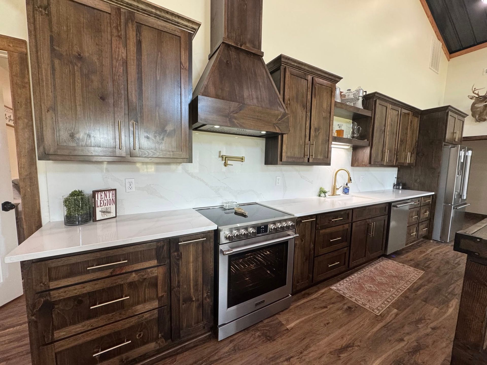 A rustic kitchen with dark stained wood cabinetry, stainless steel stove, and white stone countertops.