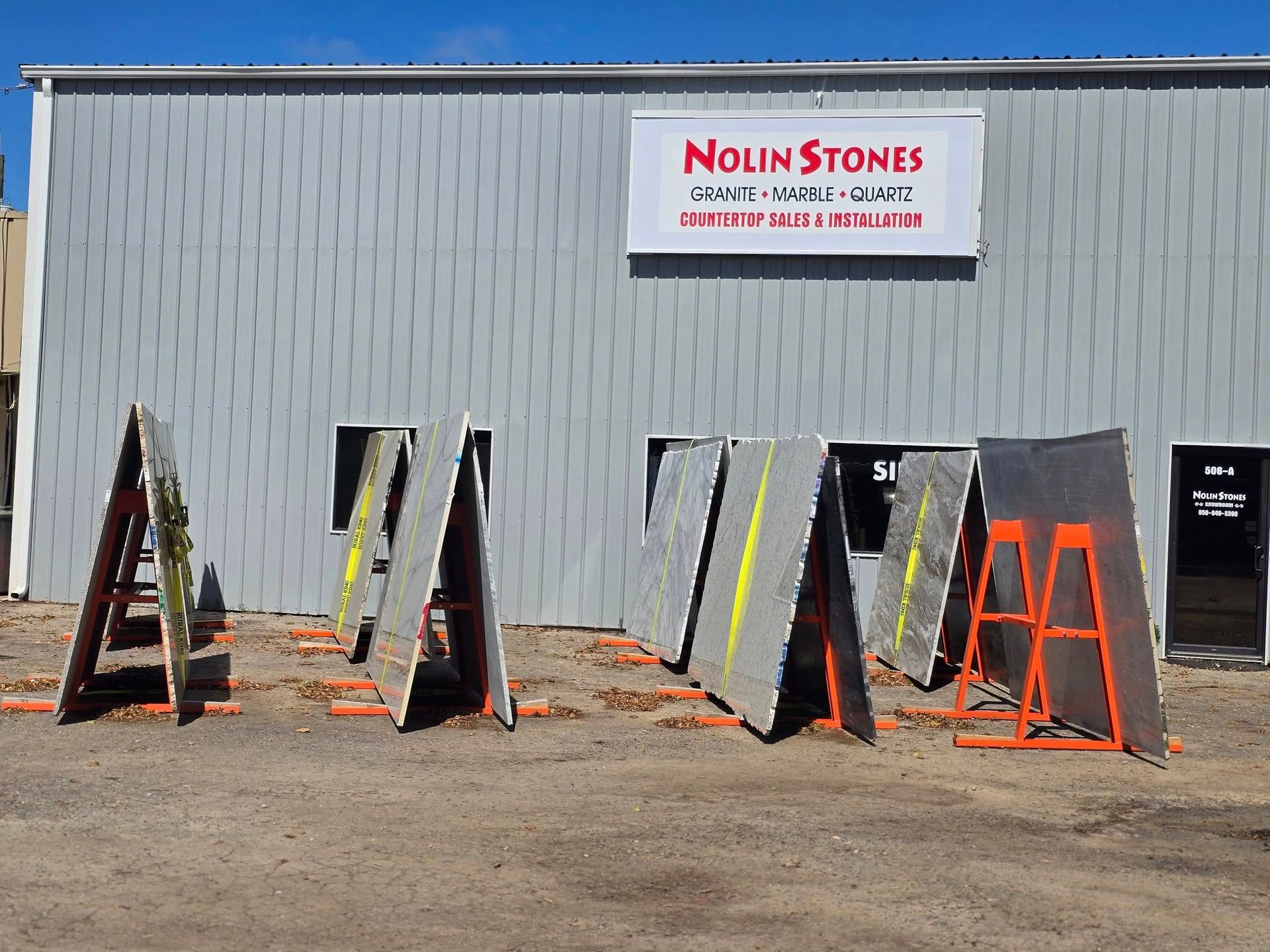Nolin Stones sign on a warehouse building exterior with several large stone slabs displayed on A-frame racks.