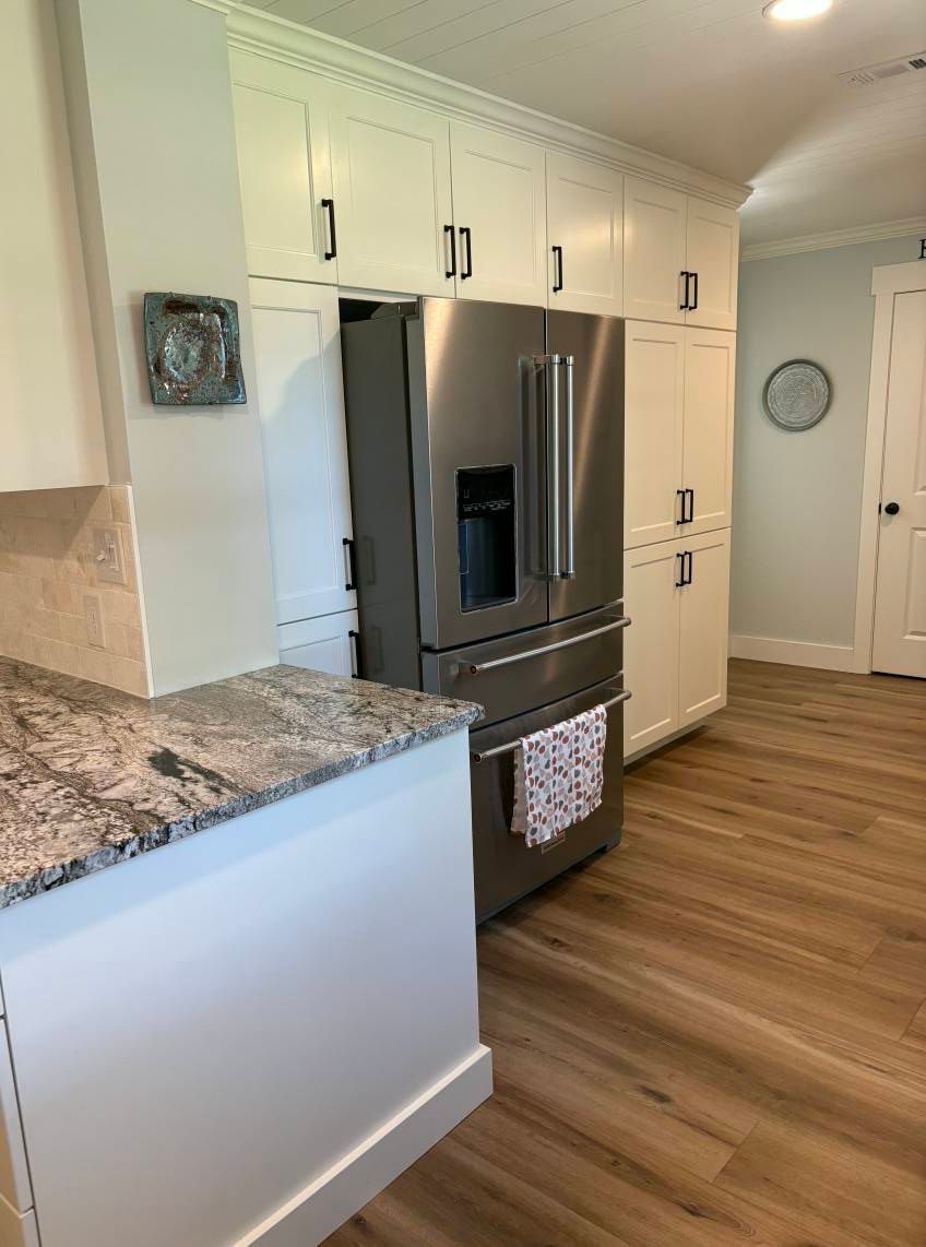 A kitchen featuring white cabinets, a stainless steel refrigerator, granite countertops, and light hardwood floors.