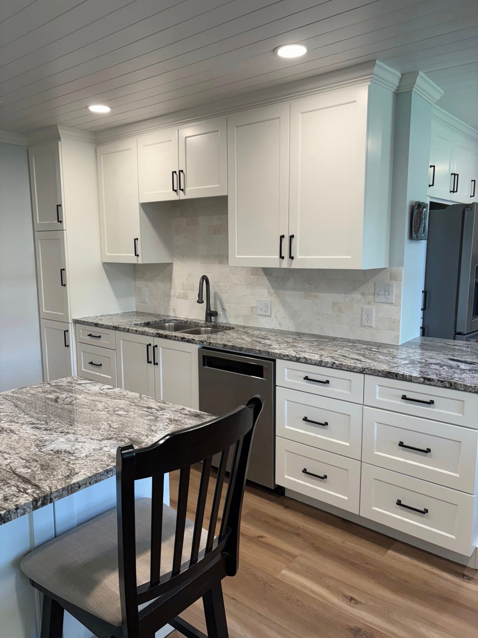 Modern kitchen with white cabinets, light granite countertops, a stainless steel dishwasher, and wood-look flooring.