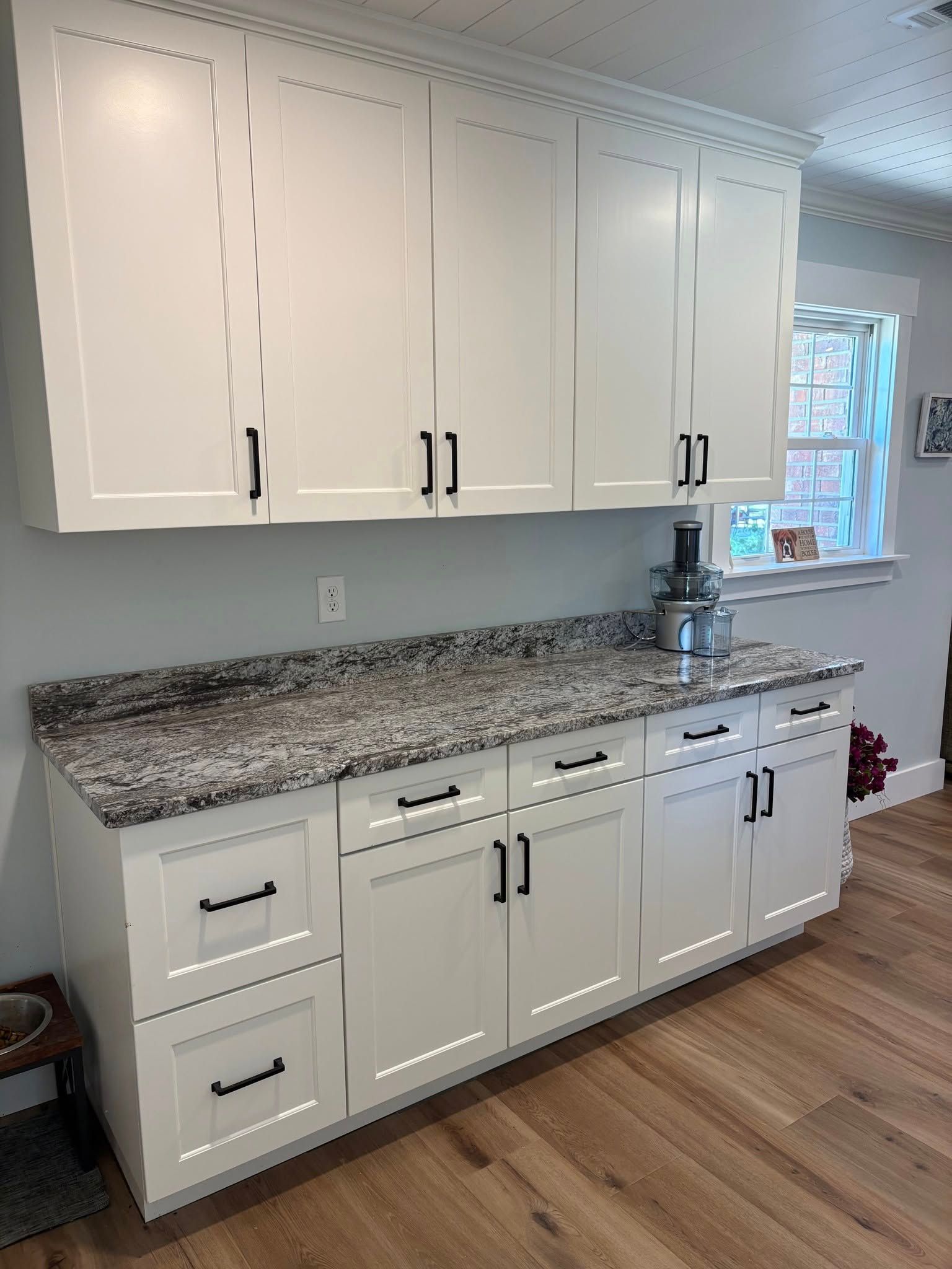 White kitchen cabinets with black hardware and speckled granite countertops, featuring drawers and lower cabinets.