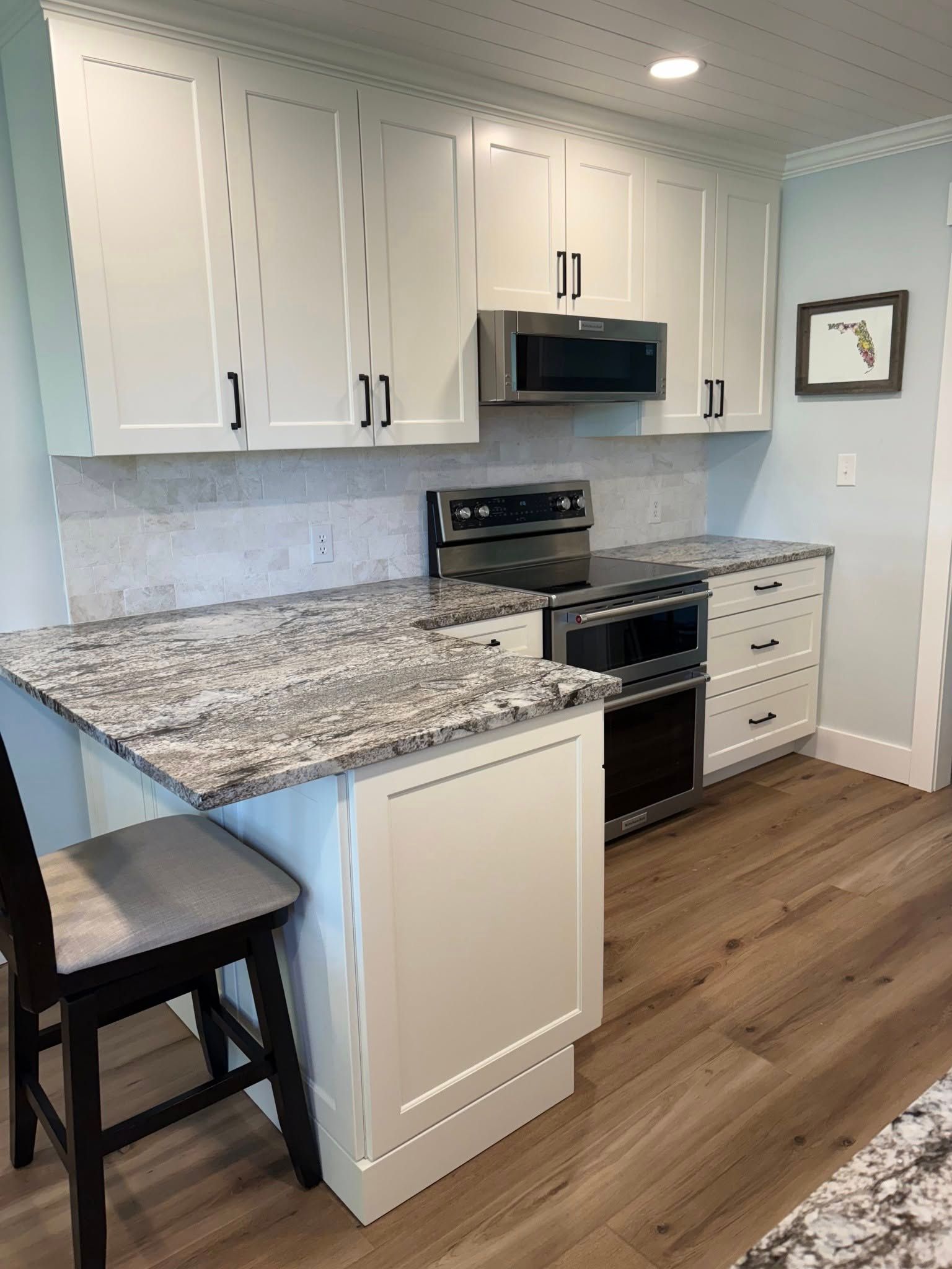 A modern kitchen with white cabinets, speckled granite countertops, a stainless steel range, and light wood flooring.