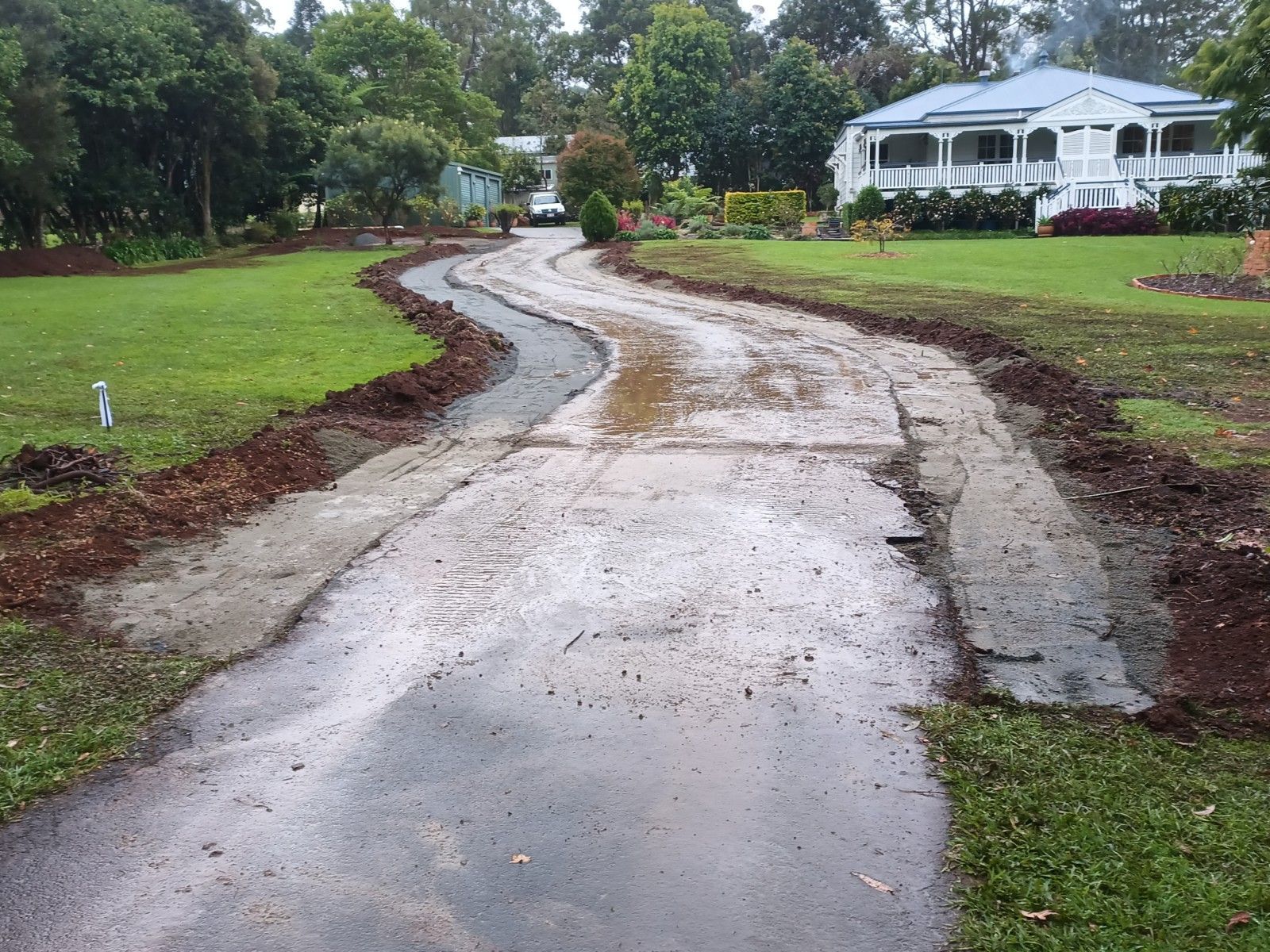 A muddy driveway leading to a house with a white house in the background.