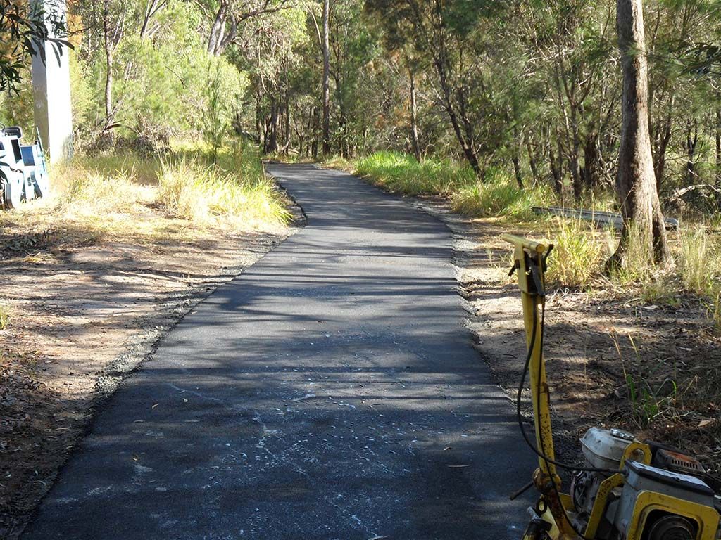 A bicycle is parked on the side of a road in the woods.