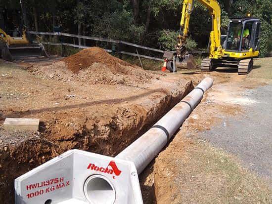 A yellow excavator is digging a hole for a pipe.