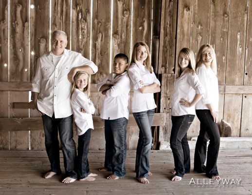 Six people in white shirts and dark pants standing barefoot against a wooden wall, posing together