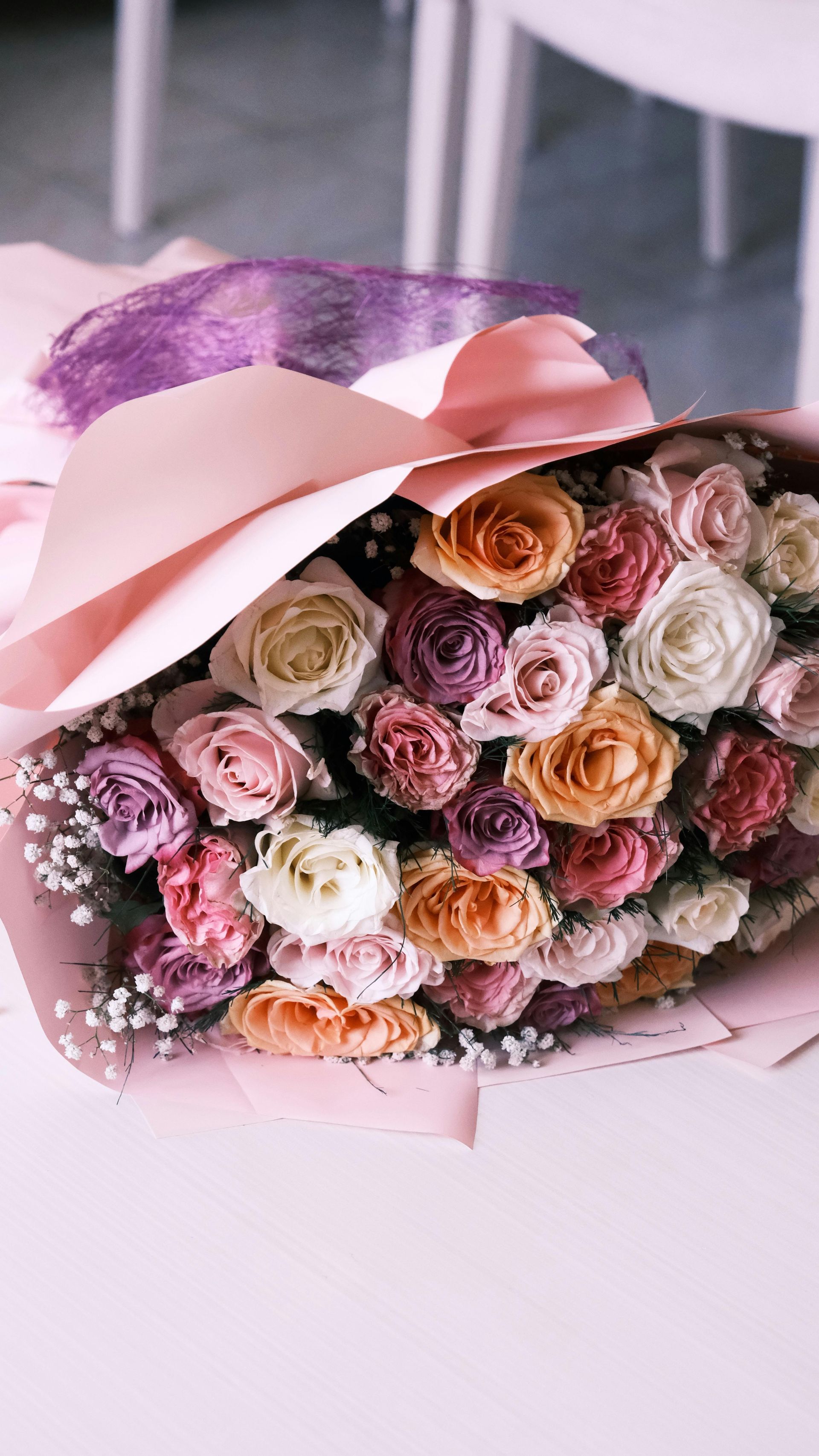 Pink and pastel rose bouquet wrapped in paper with a large ribbon on a white table