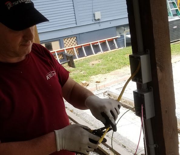 Electrician in red shirt and gloves working on wiring inside two electrical boxes.