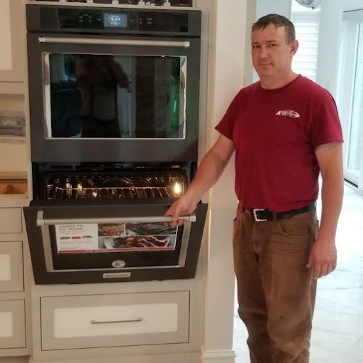 Man in red shirt opens a built-in oven in a kitchen.