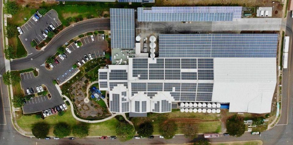Aerial view of a building with solar panels, a parking lot, and green landscaping.