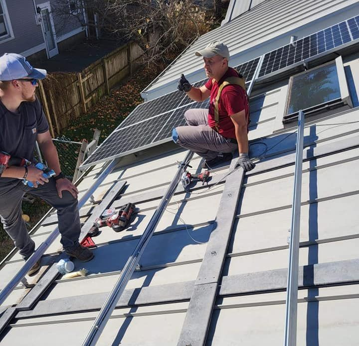 Two people installing solar panels on a roof; one points up, another observes; sunny day.