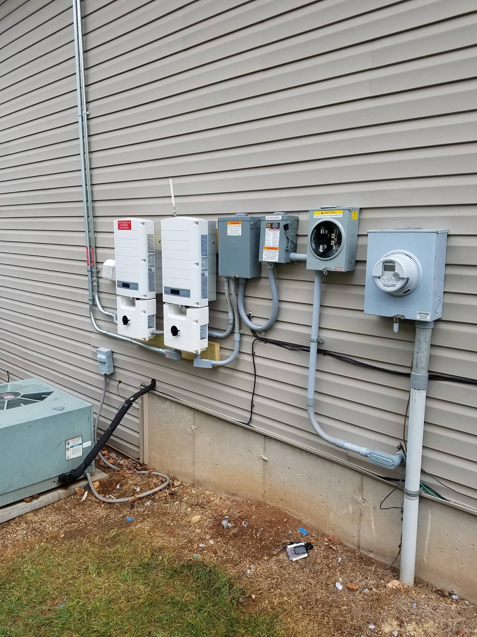 Outdoor electrical equipment on a house exterior, including solar inverters, a meter box, and conduit.