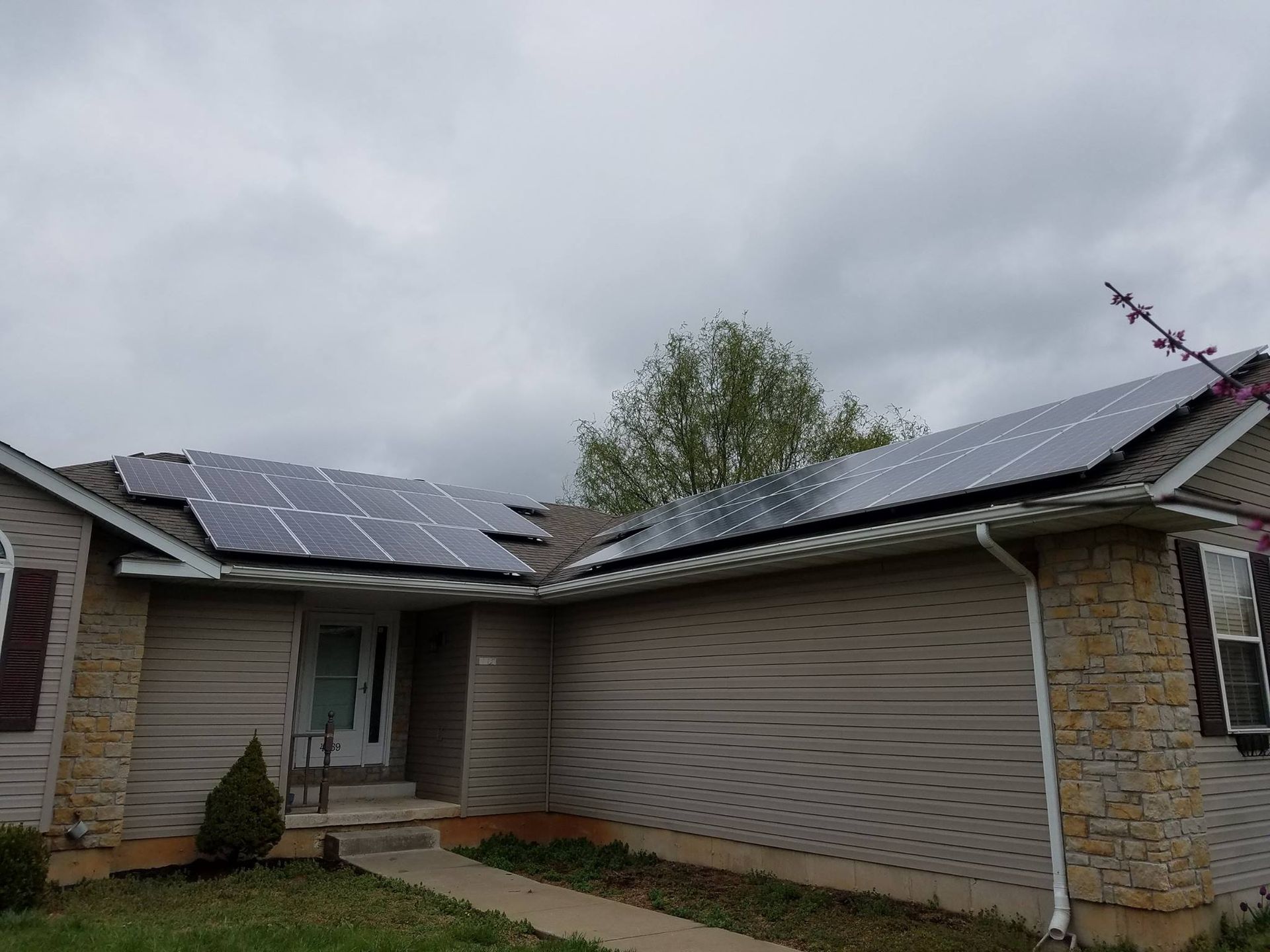 House with solar panels on roof, cloudy sky.