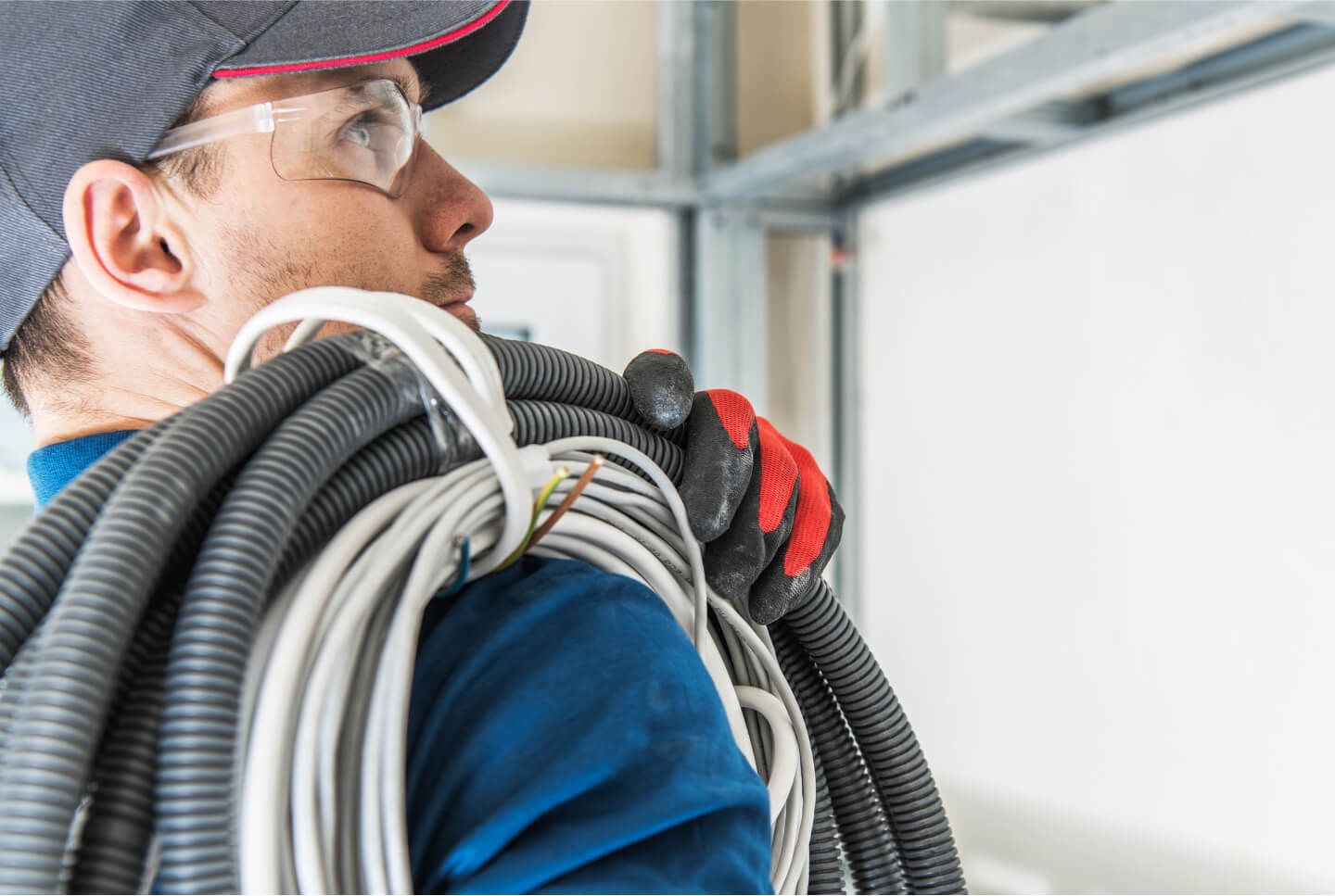 Electrician carrying coiled electrical cables in a construction site.