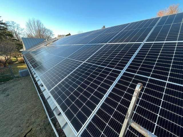 Solar panels on a sloped roof under a clear blue sky. A ladder is present.