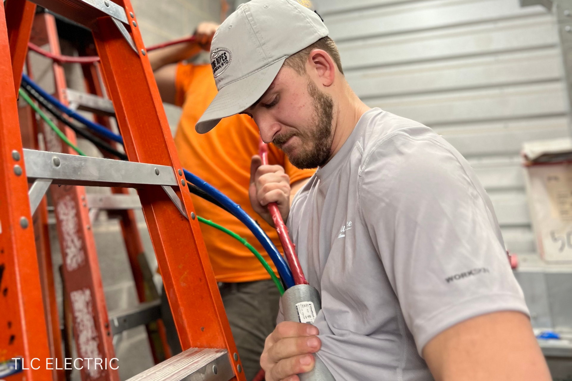 A man is sitting on a ladder working on electrical wires.