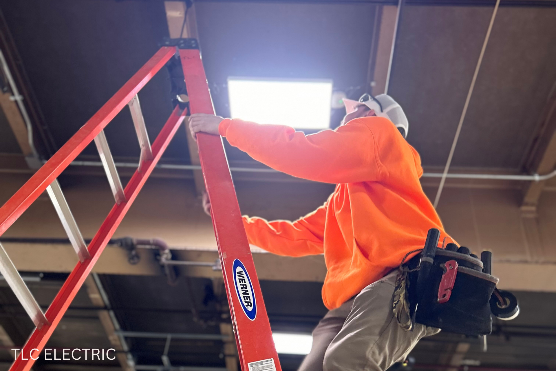 A man is standing on a ladder that says tlt electric