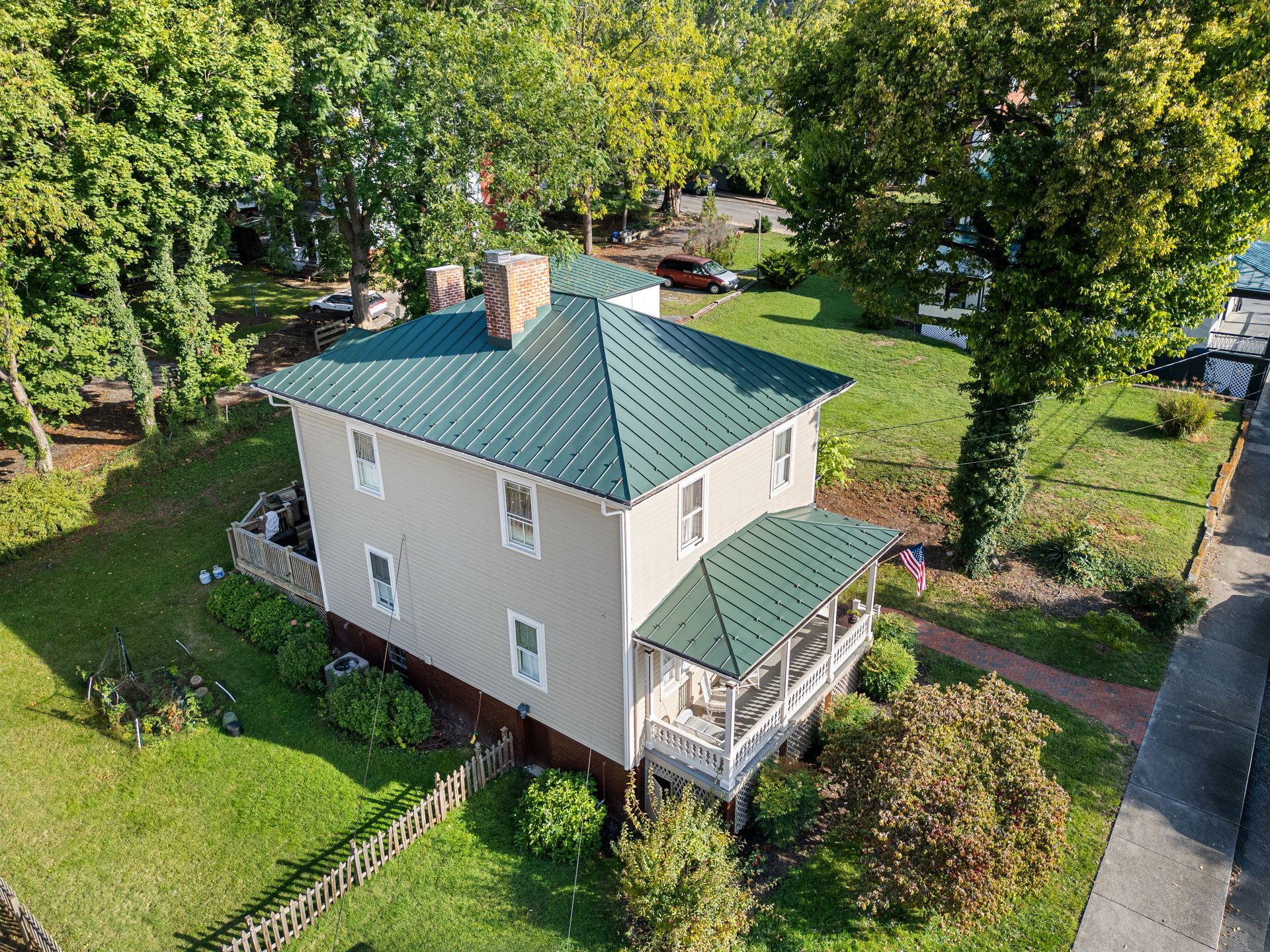 An aerial view of a white house with a green roof surrounded by trees.