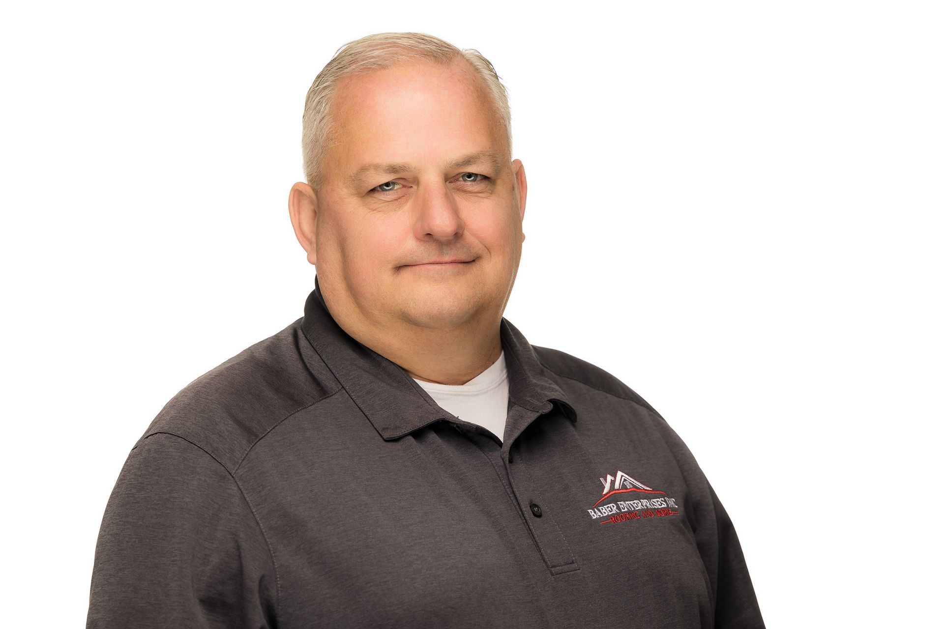 A man in a gray shirt is smiling for the camera on a white background.